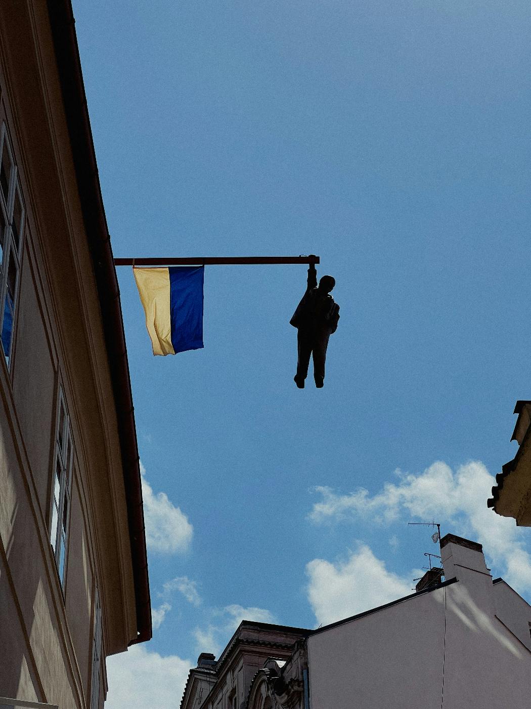 A flag pole off a building with a statue of a man holding on to it