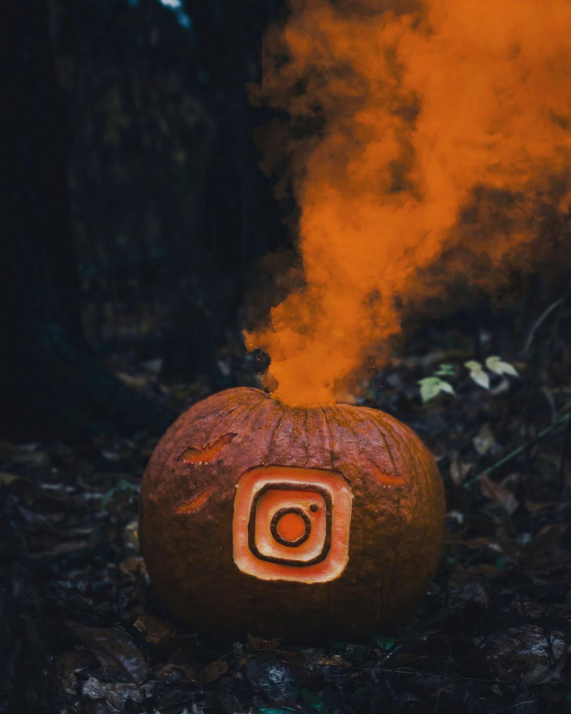 A pumpkin with the Instagram icon carved in it and orange smoke coming out 