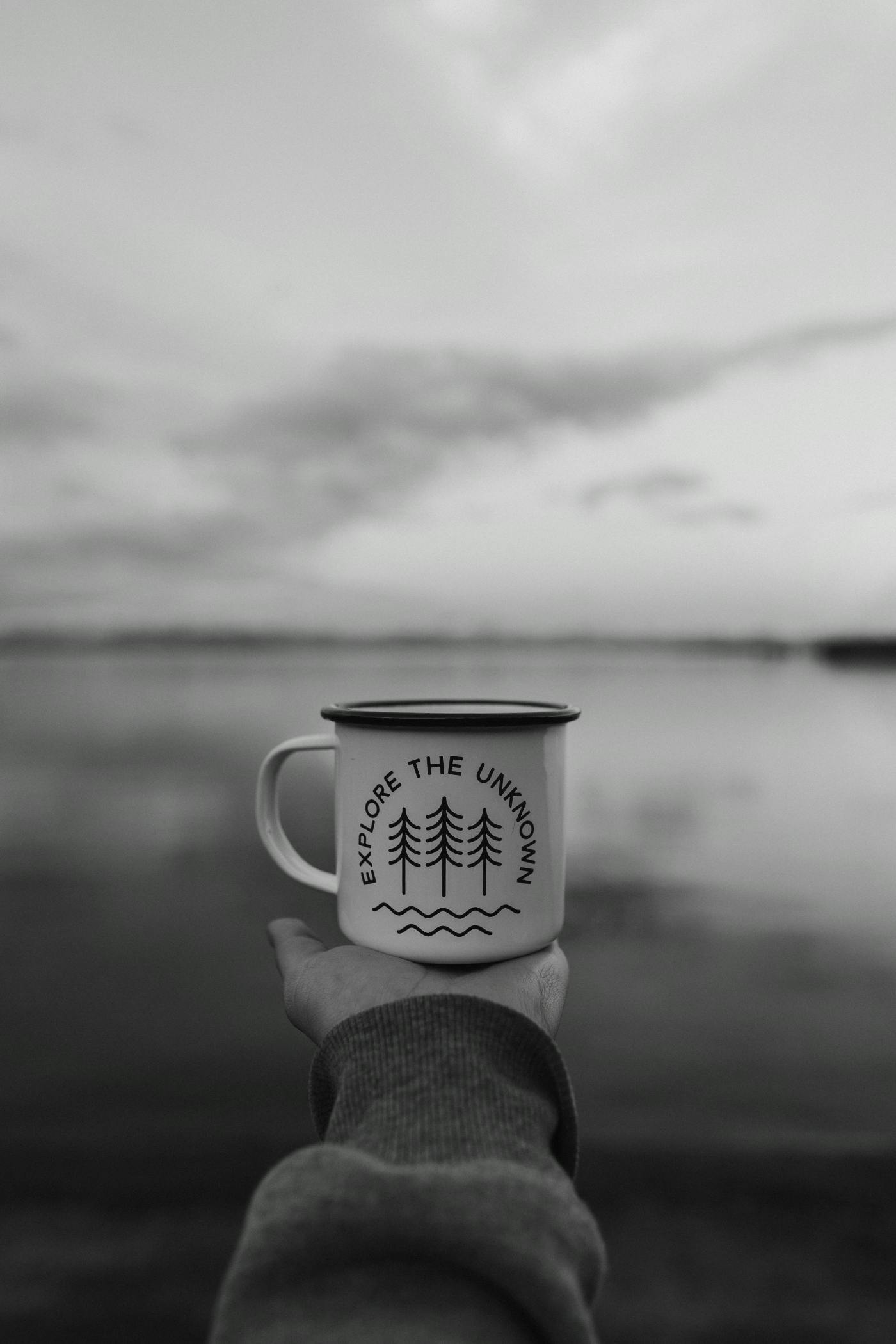 A hand stretchng out to the horizon holding a cup that reads explore the unknown