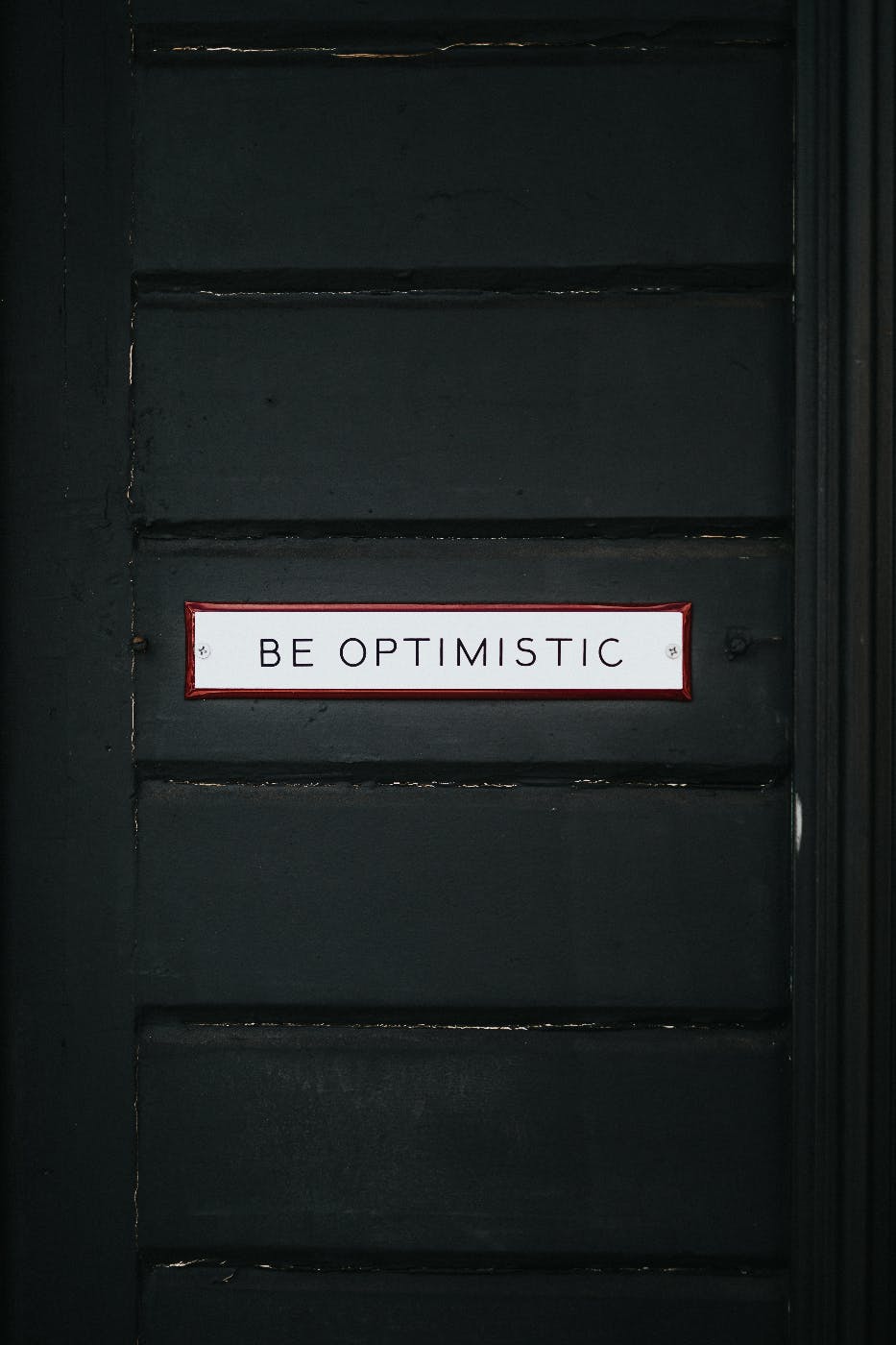 A black door with the words be Optimistic on it