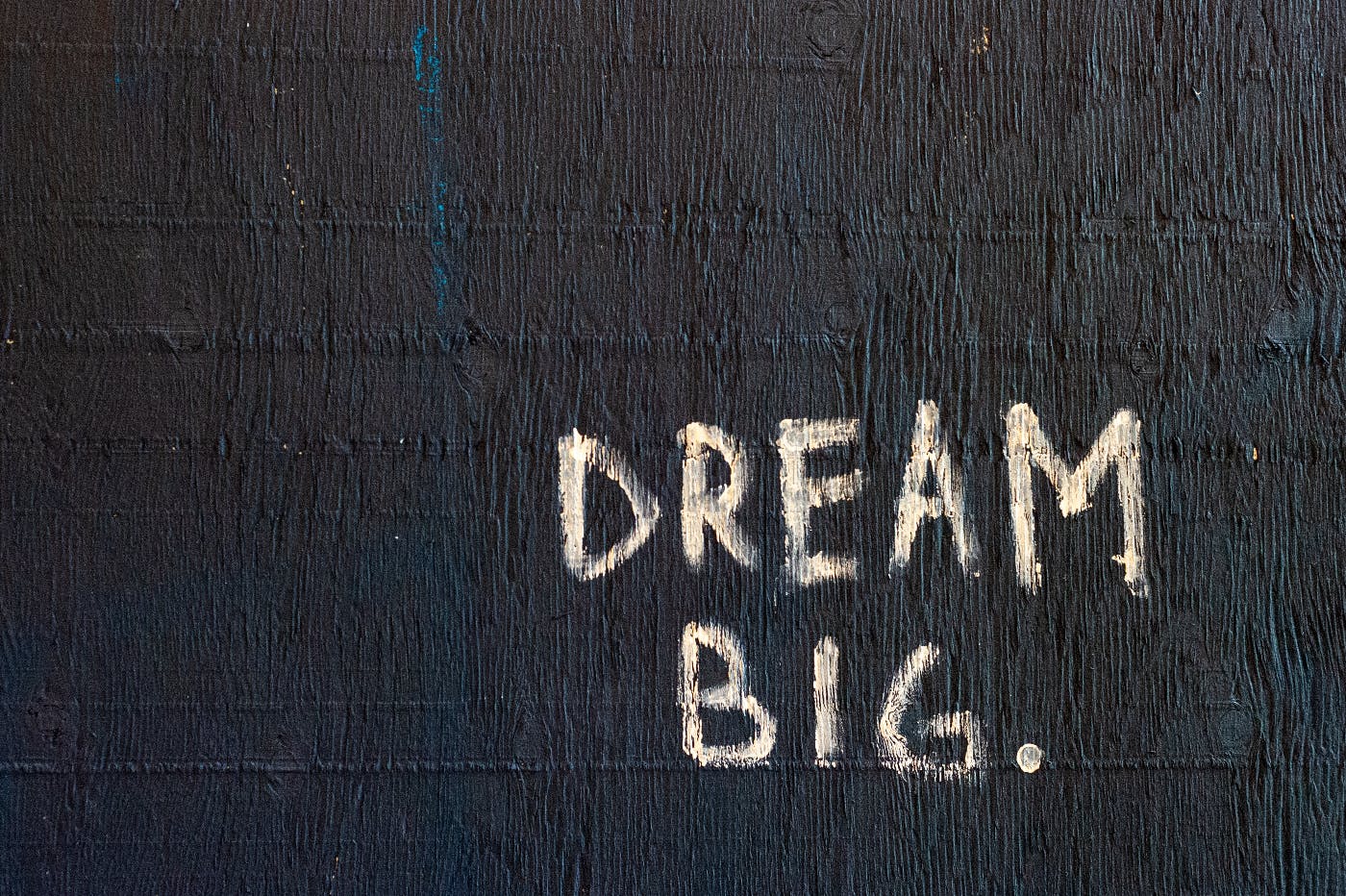 A highly textured black and blue wall with Dream Big painted on it