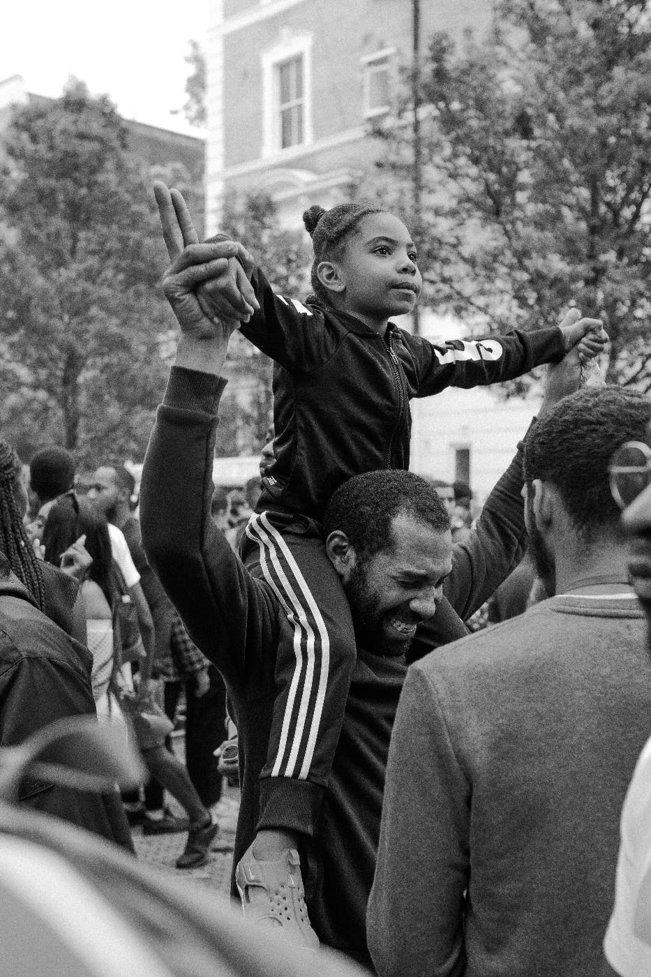 A celebration in the streets a black man has a child on his shoulders