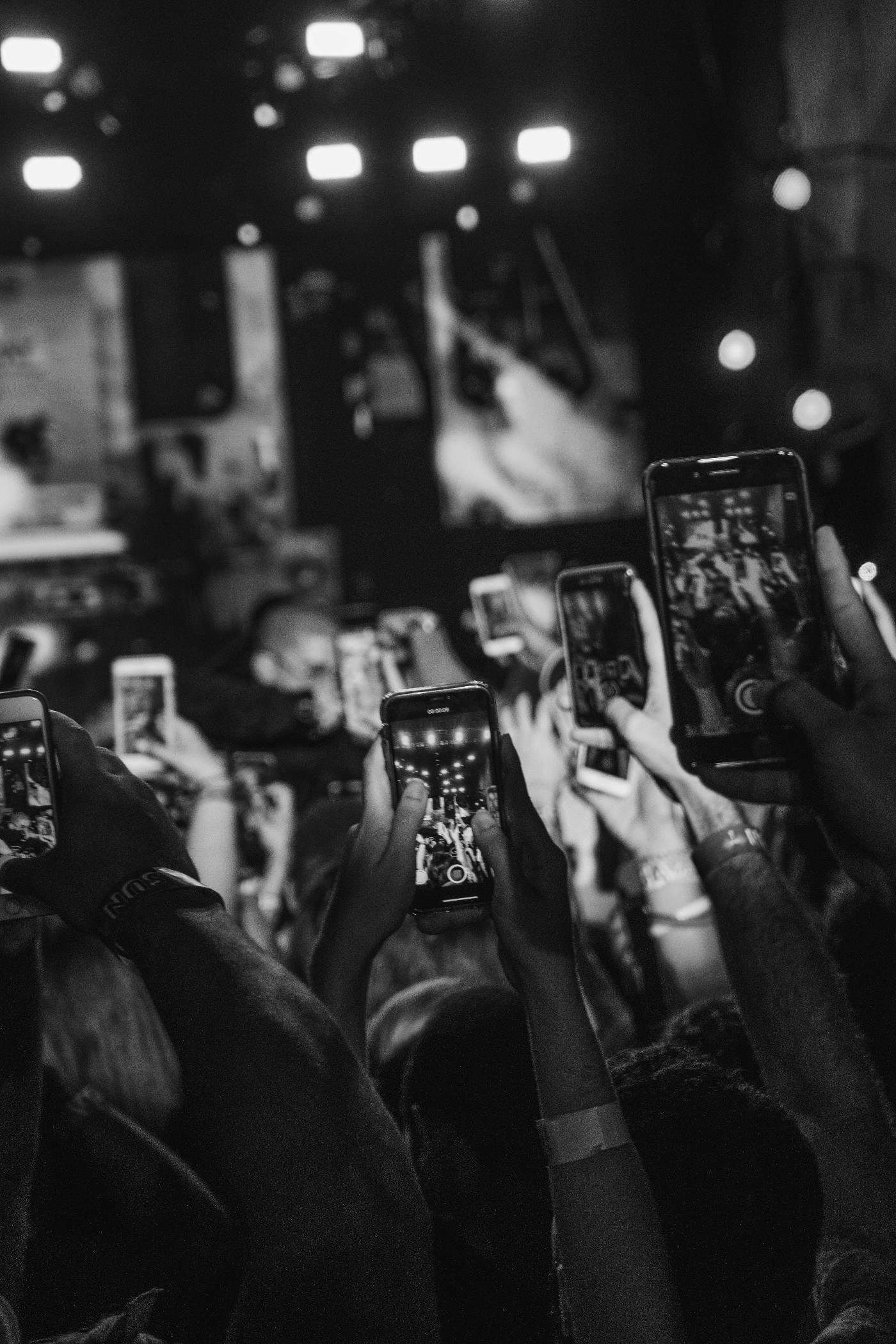 Many people holding up their phones and filming a concert