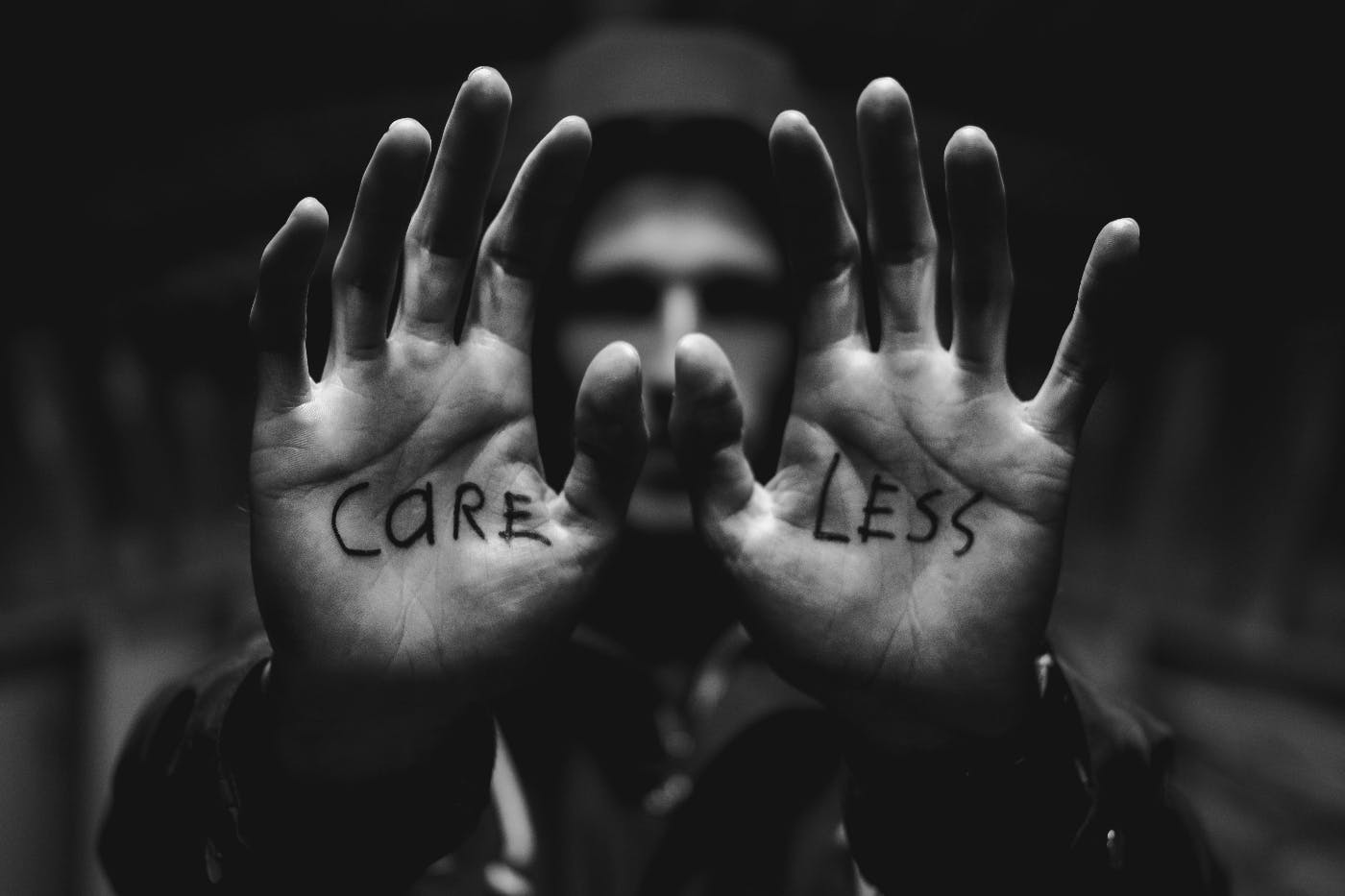 A man in a hoodie holding up his hands, written on the right is "care" on the left "less"