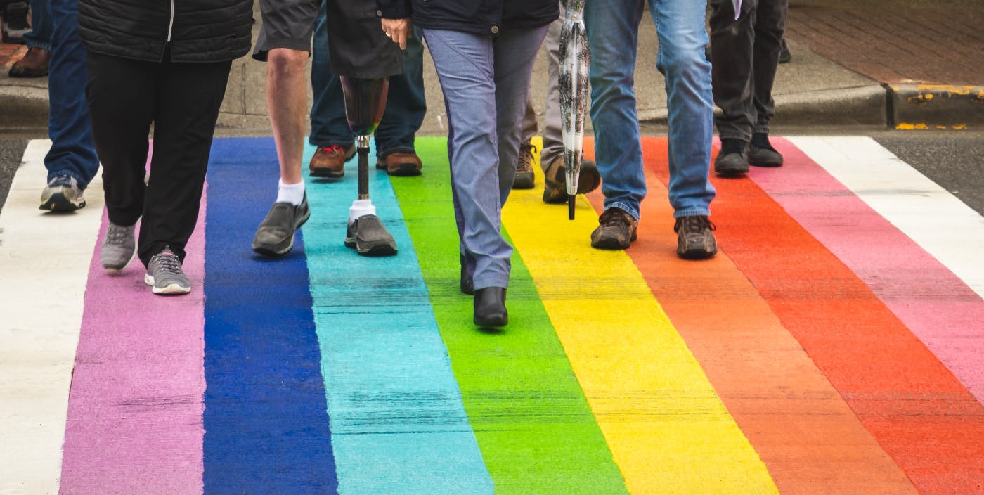 Different people using a rainbow crosswalk, one person has a prosthetic leg