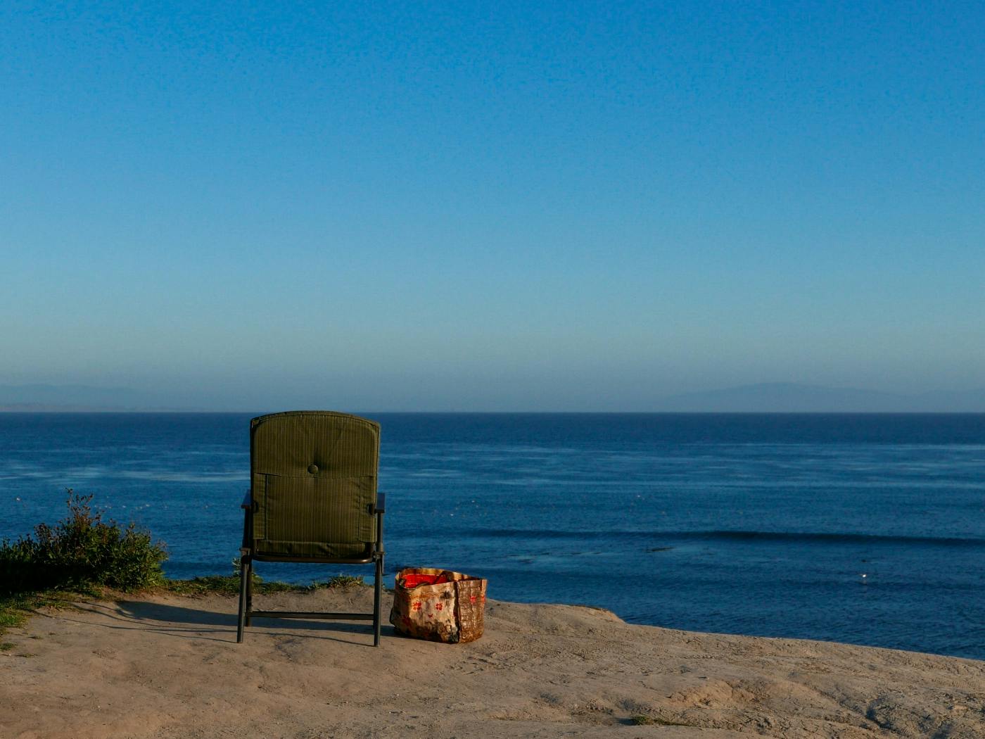 A chair and a bag on a hilll overlooking a blue ocean