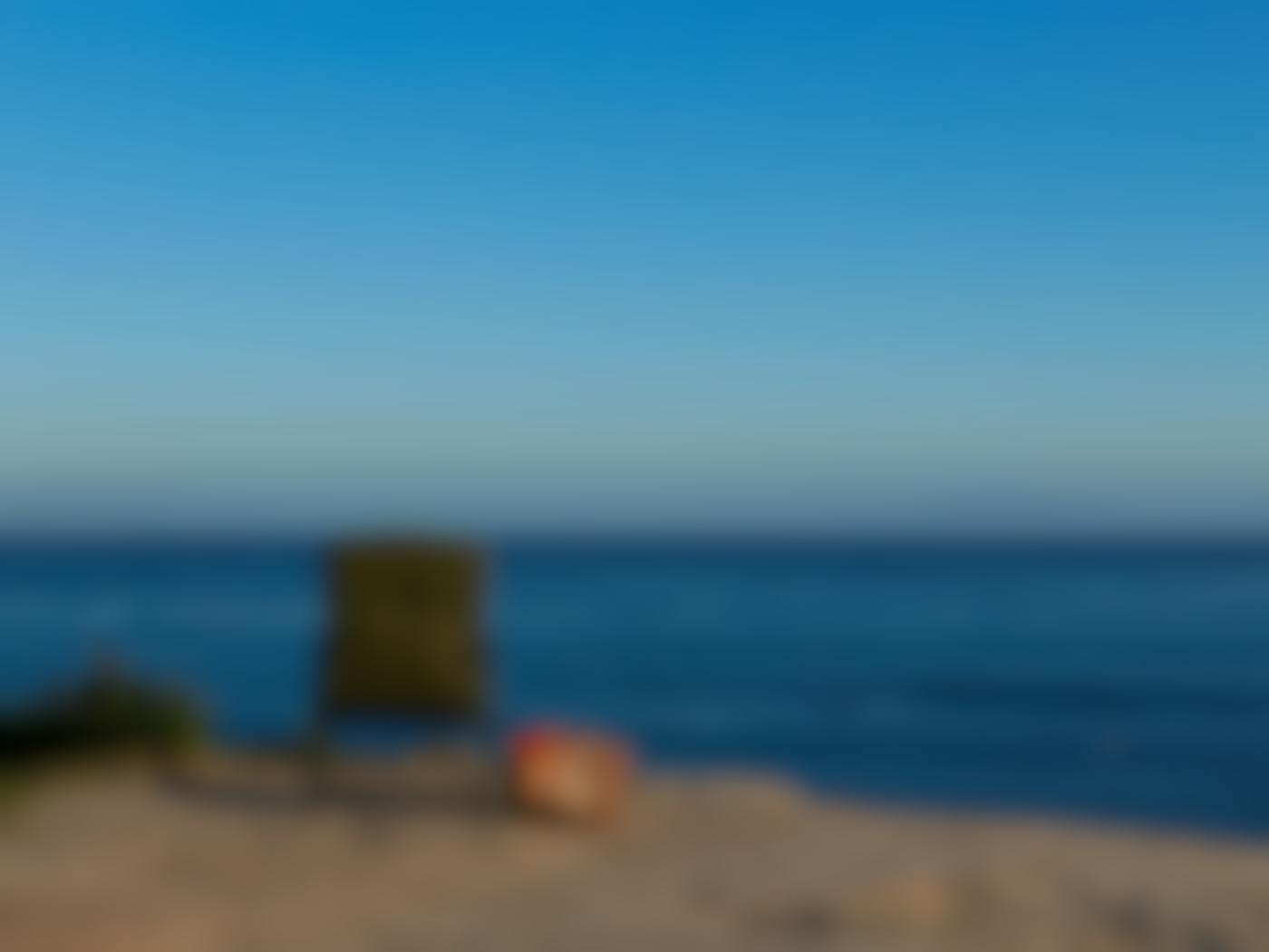 A chair and a bag on a hilll overlooking a blue ocean