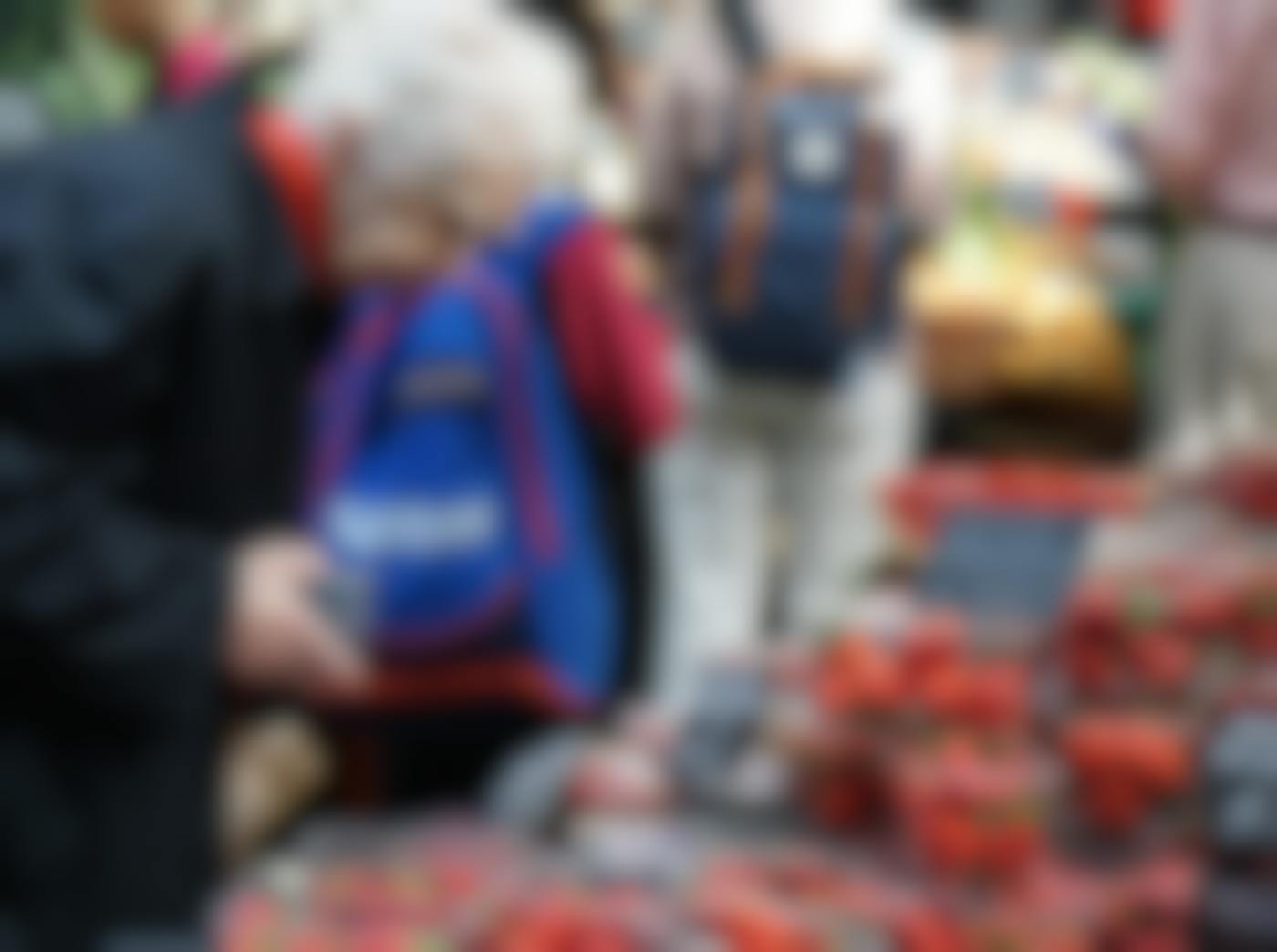 An elderly woman choosing containers of strawberries at a crowded open market