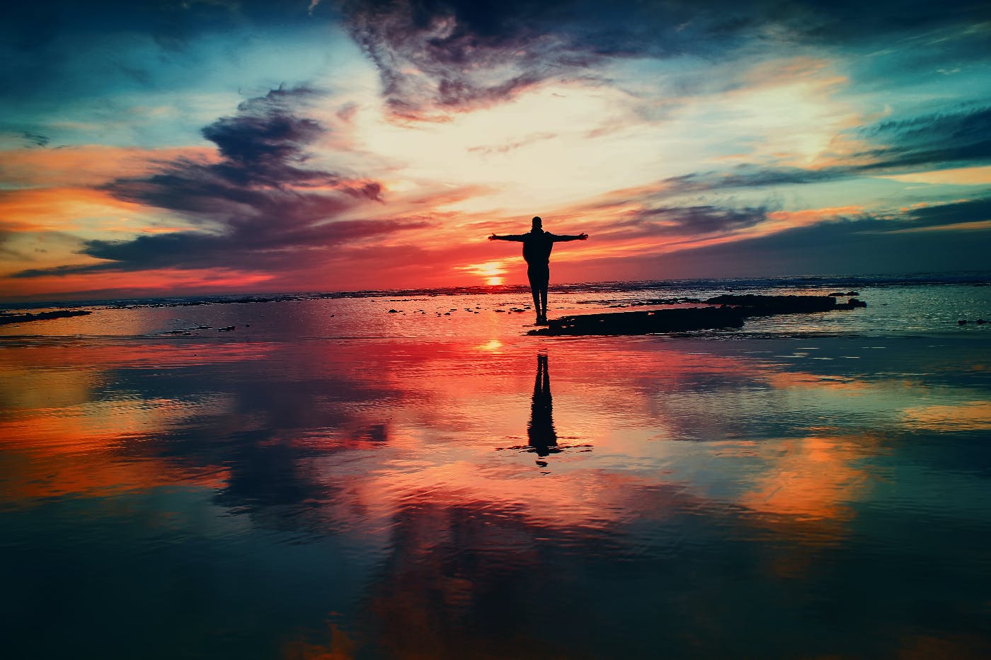 Silhouette of a man stainding on a rock surrounded by water which is refelcting the sunset