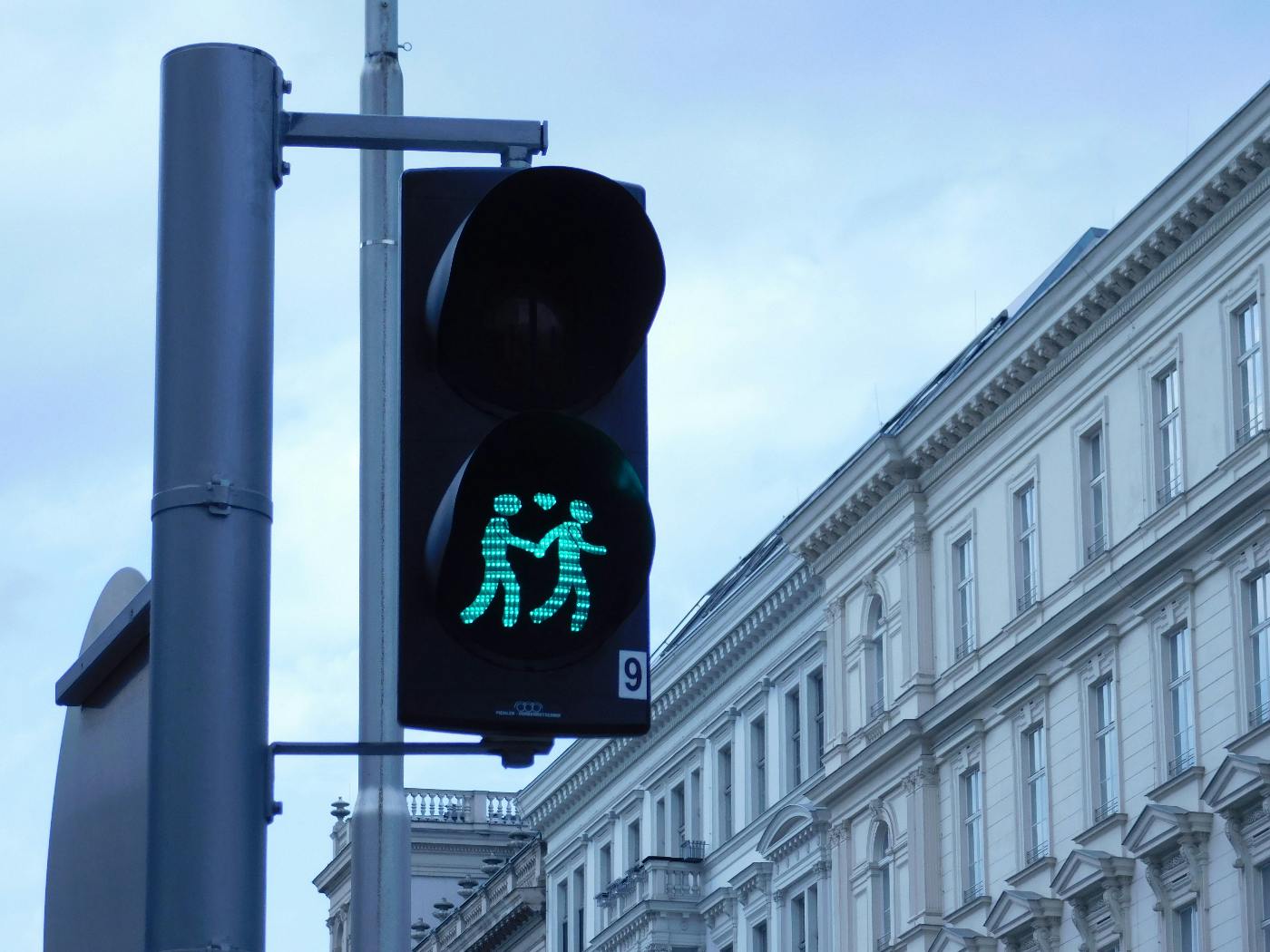 A traffic light with the bottom light displaying a couple holding hands and a heart between them.