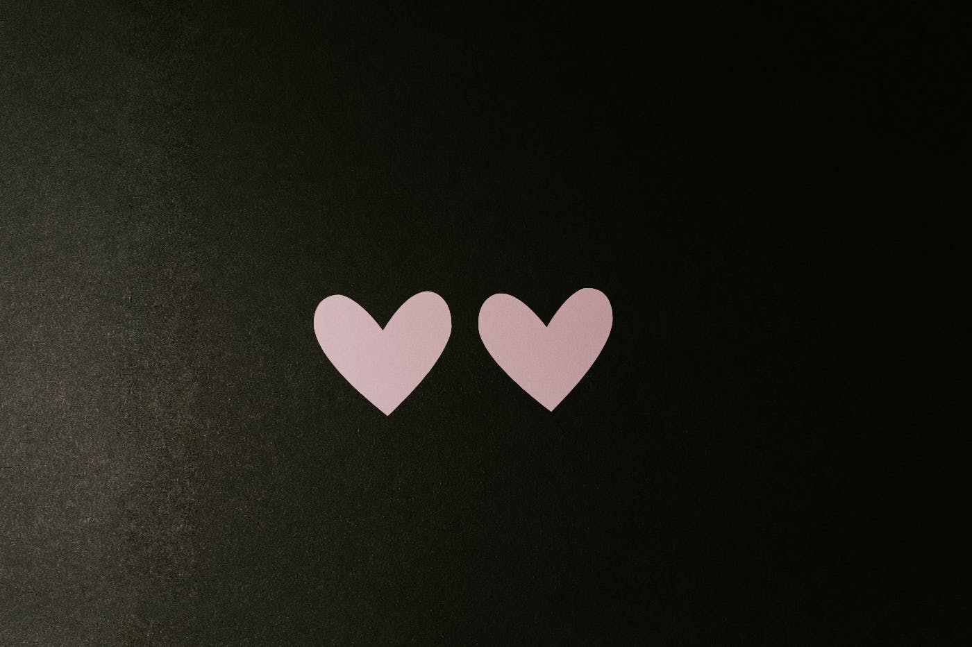 Two pink paper hearts on a black background