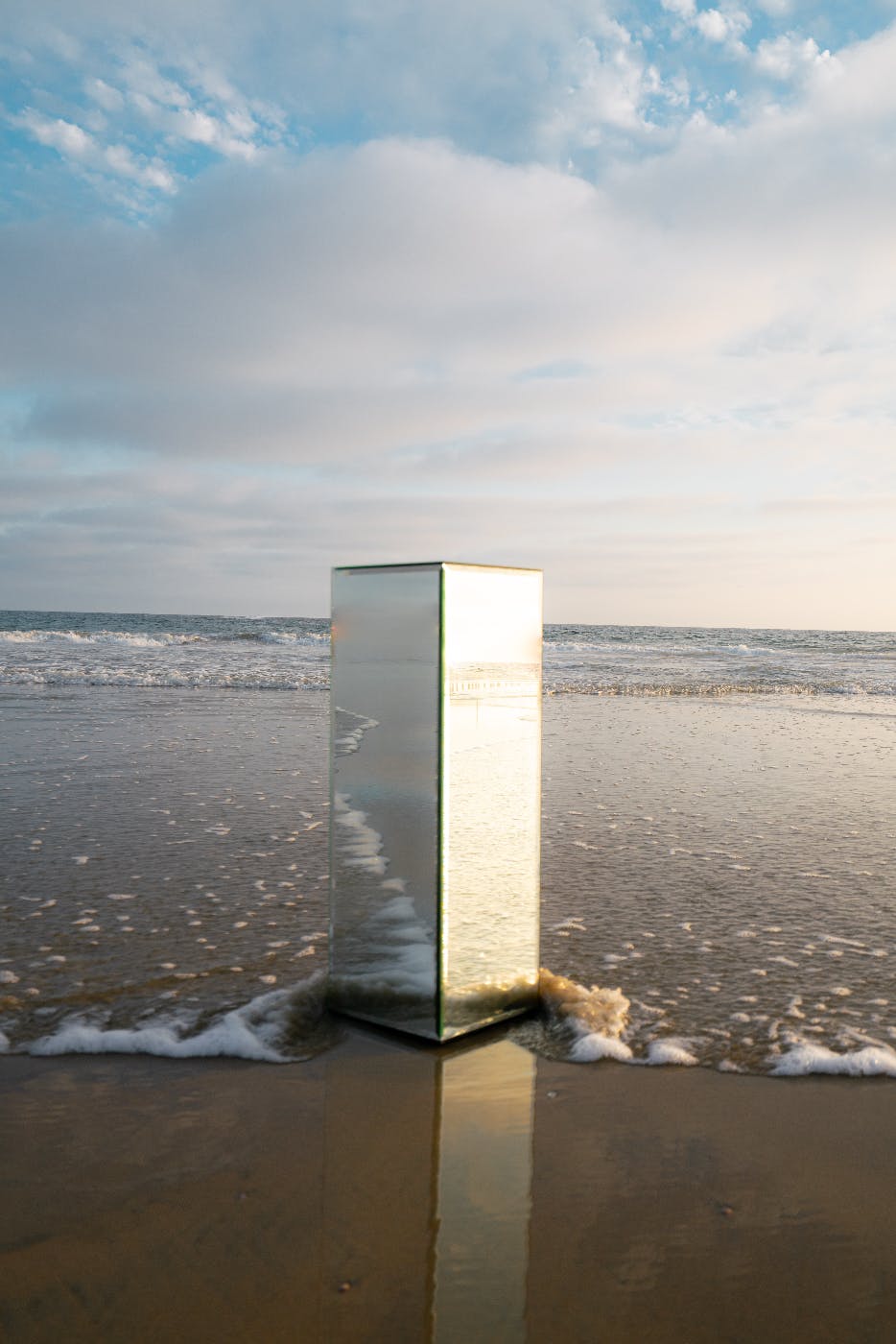a reflective rectangular column sitting in the ocean surf