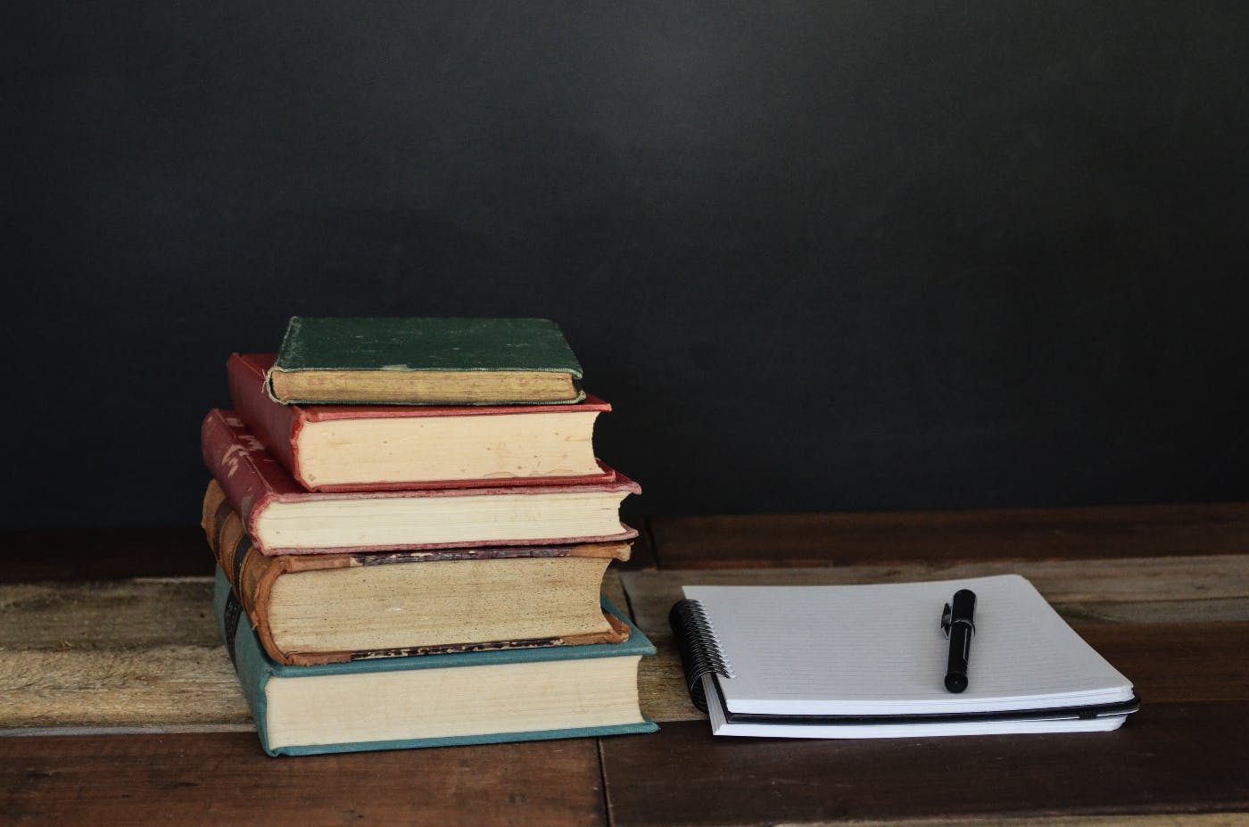 a pile of books next to a note pad and pen