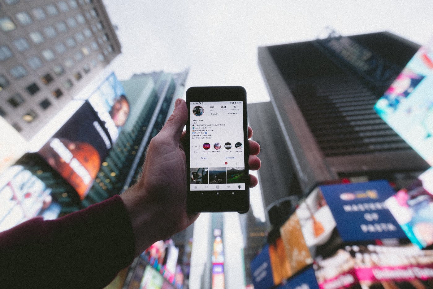 a hand holding up a smartphone in the middle of Times Square