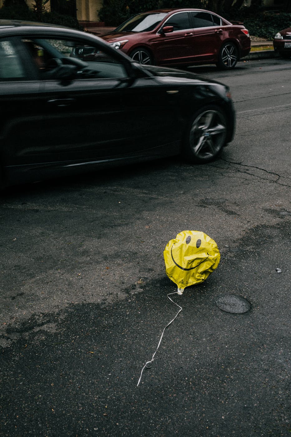A deflated smiley face balloon sitting near traffic