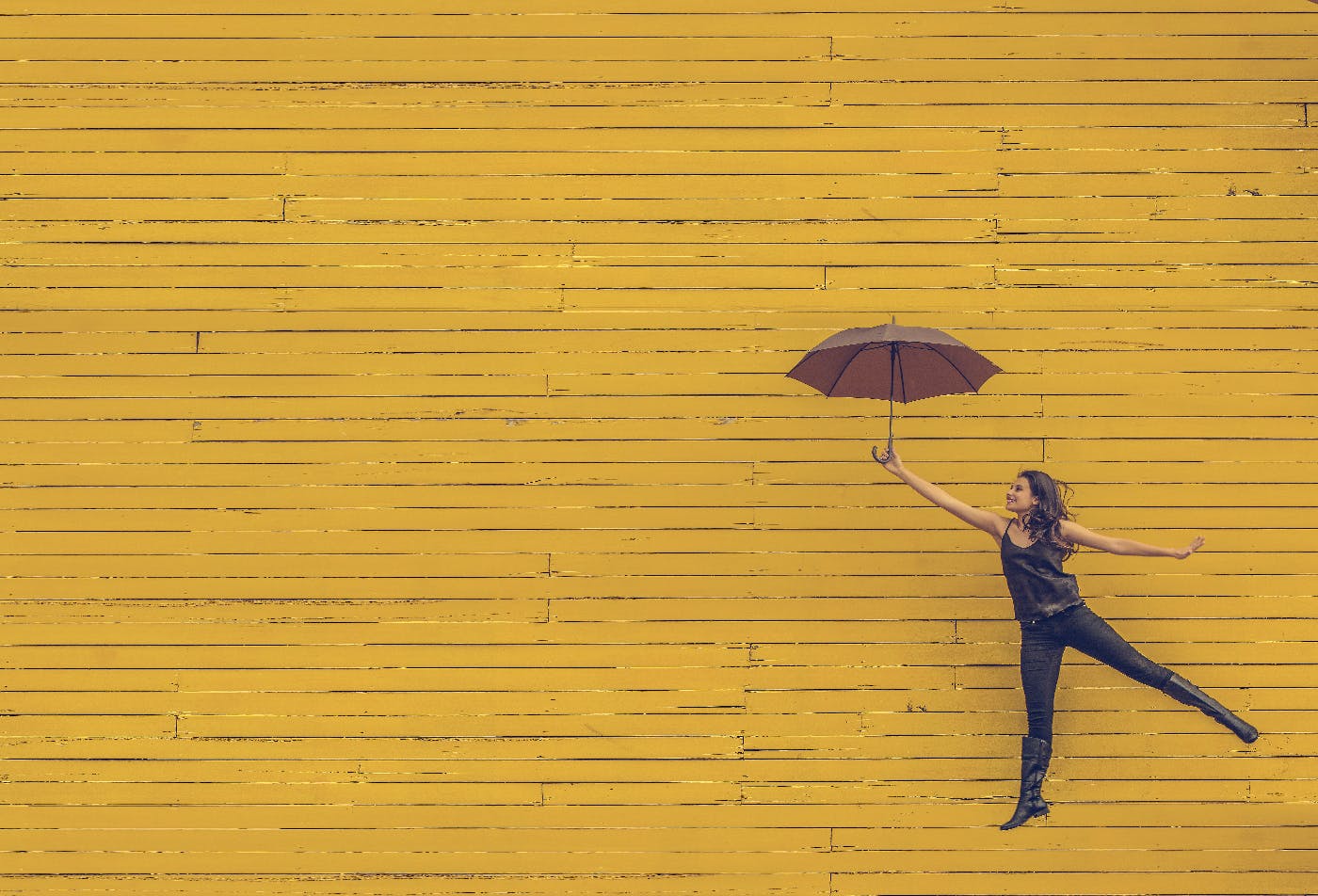 A woman with an open umbrella seeming to float in front of a yellow wall
