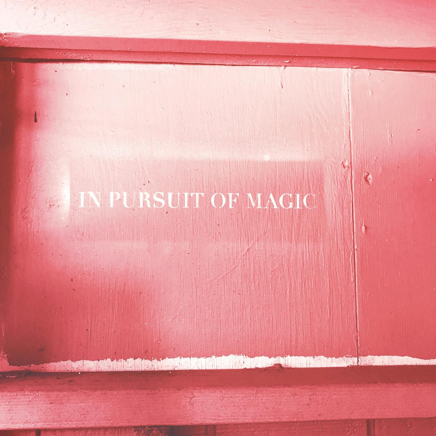 A pink wall with the words In Pursuit of Magic stenciled on it in white