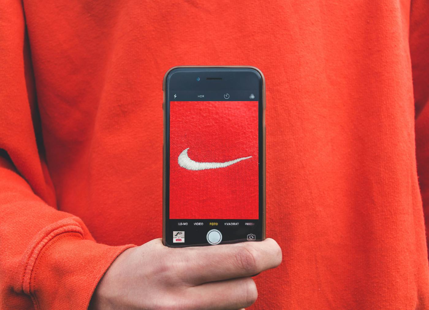 a person in a red shirt holding up their smartphones screen that has a Nike label in the exact red