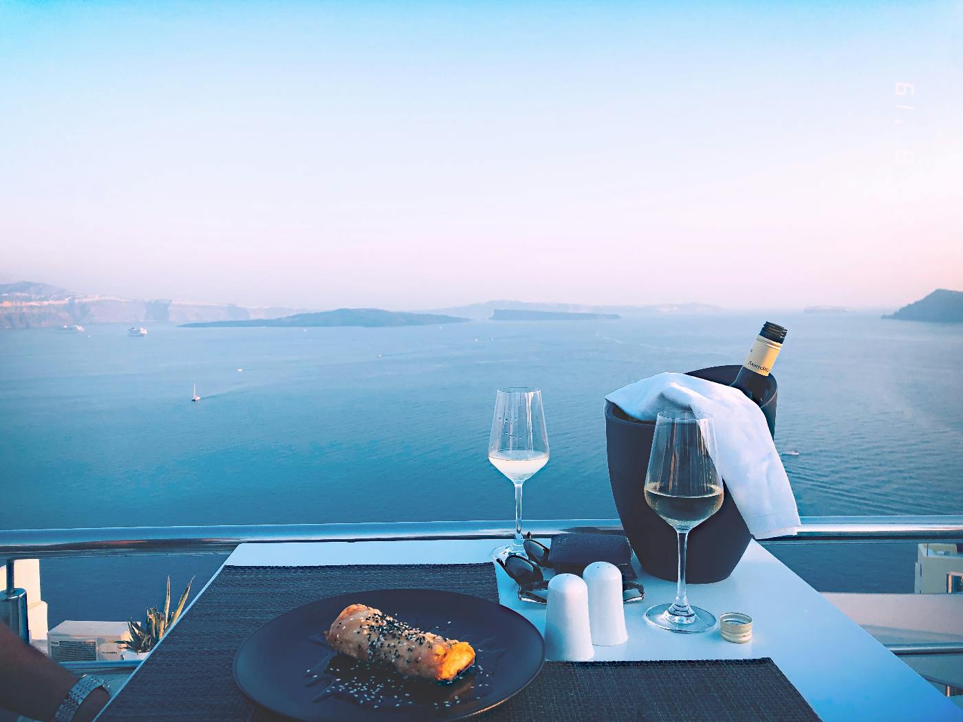 A table set for dinner, two wine glasses a bottle in wine bucket overlooking the ocean