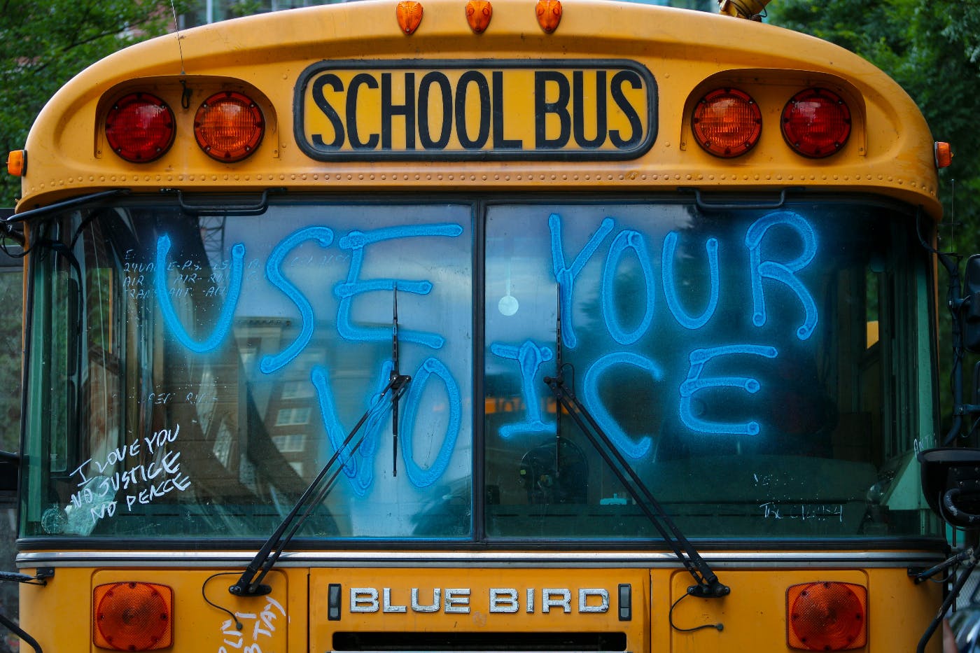 The front of a school bus with the words Use Your Voice in blue painted on the windshield