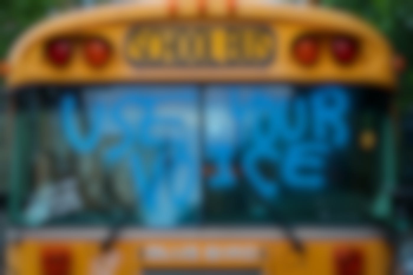 The front of a school bus with the words Use Your Voice in blue painted on the windshield