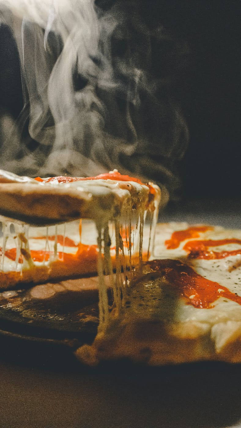 A slice of pizza being pulled from the rest of the pie, steaming and gooey with cheese