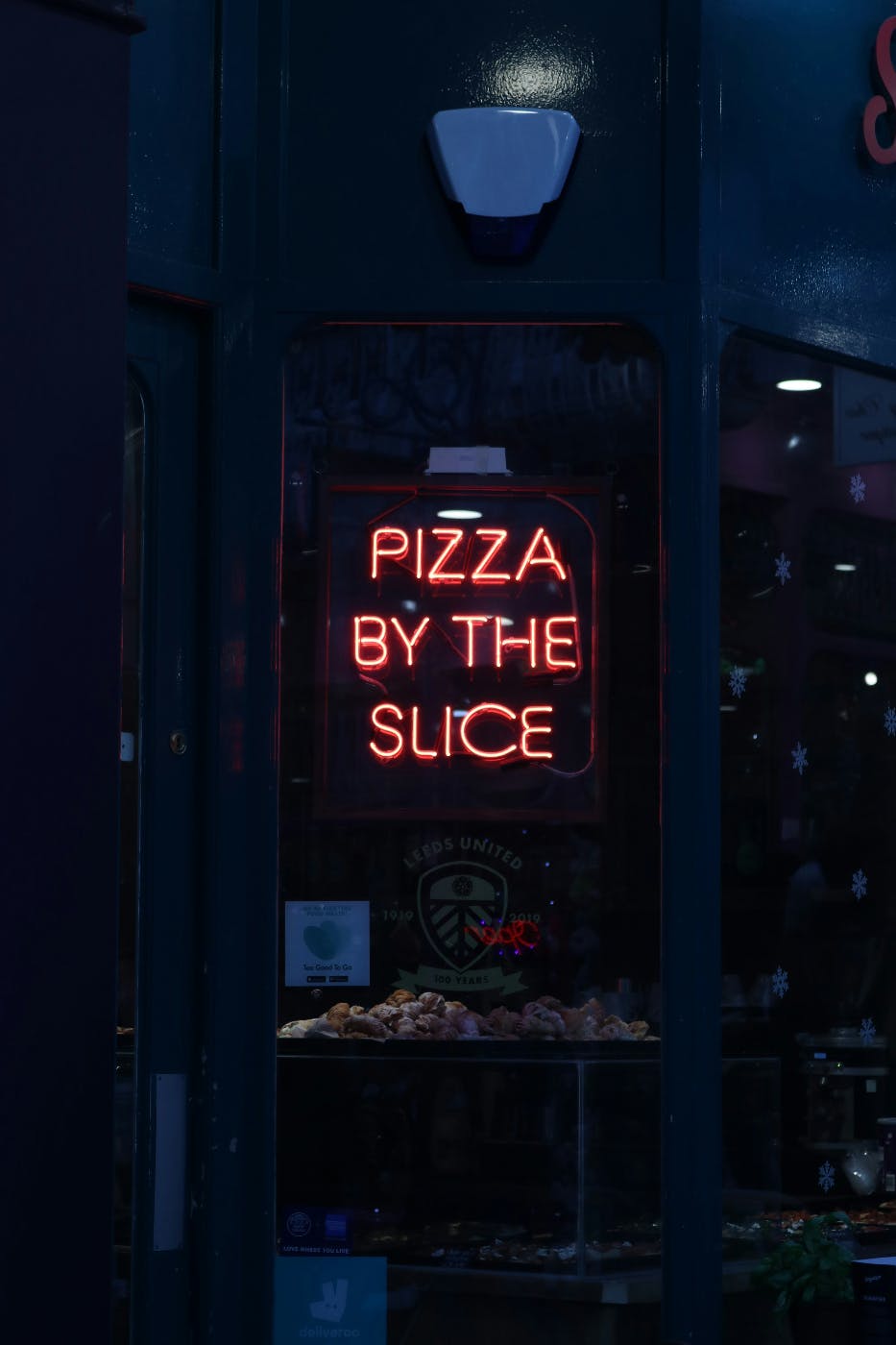 A neon sign in a shop window Pizza by the Slice