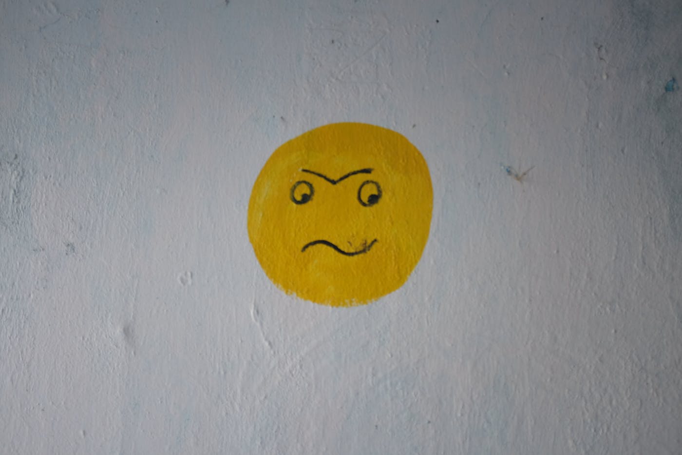a grey wall with a yellow face with a perplexed looked painted on it