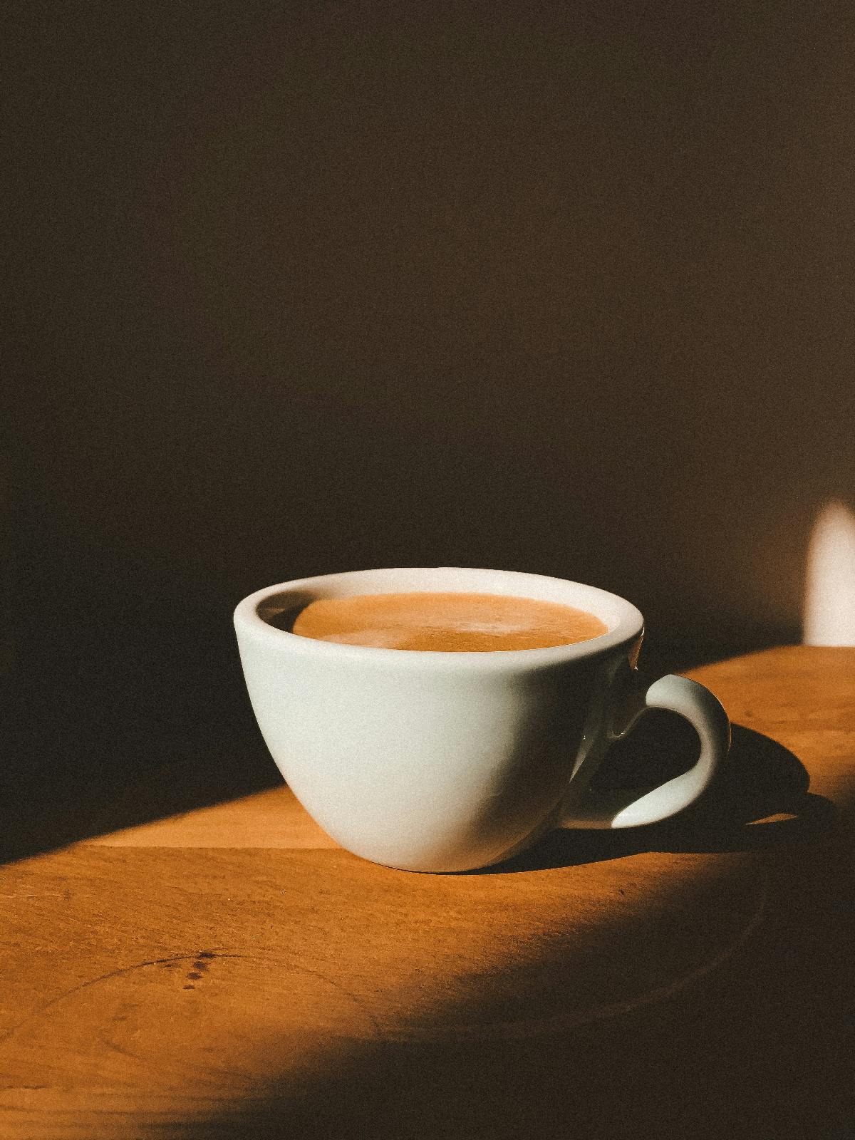 a white coffee cup sitting in a slash of sinlight in a dark room