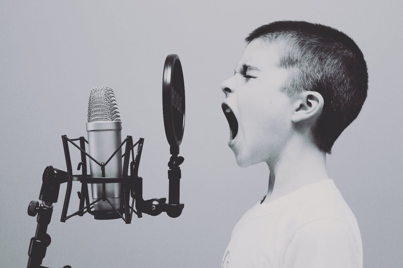 A kind in front of a pop screen and a mic singing