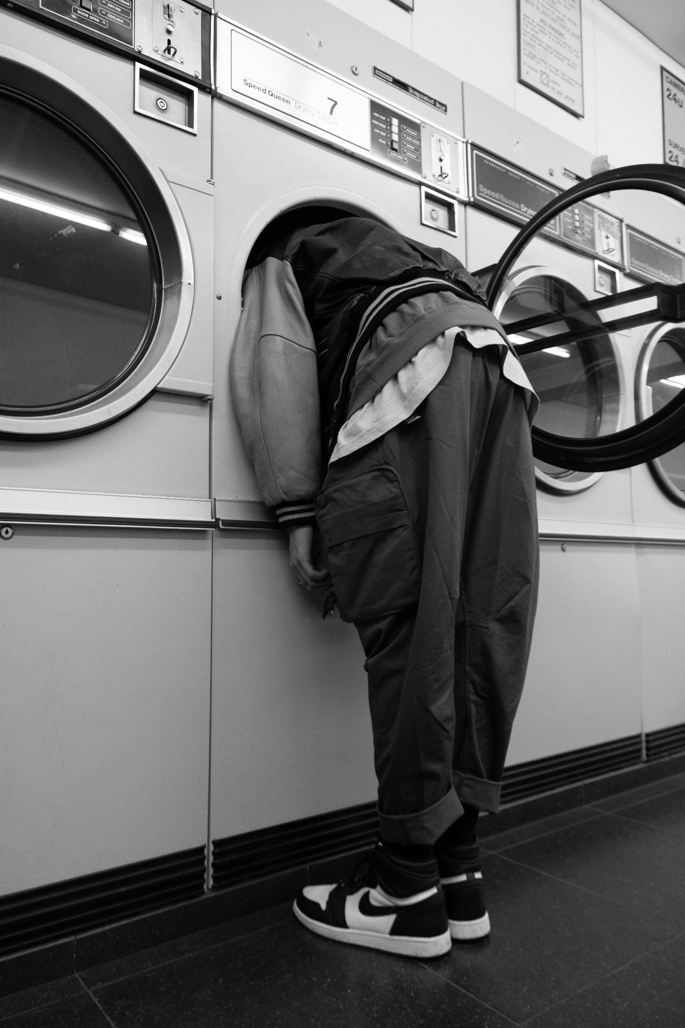 A fully dressed person with their head inside a laundromat dryer