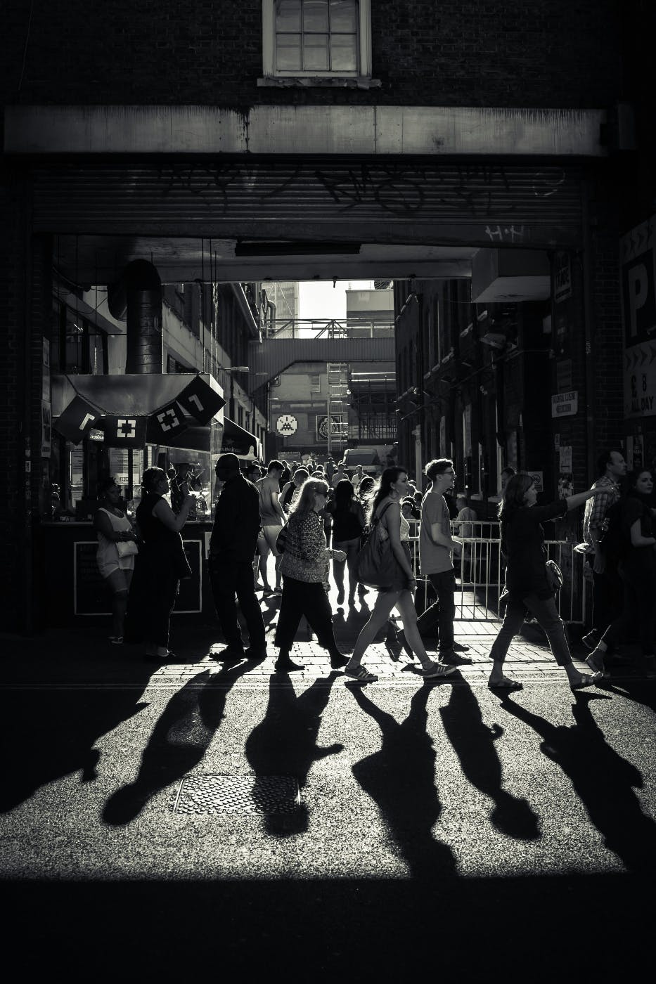 Grey scale image of a crowd crossing a street in front of a marketplace