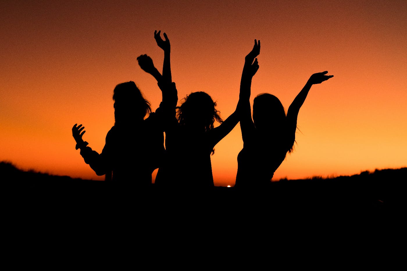 Three people in silhouette dancing at sunset