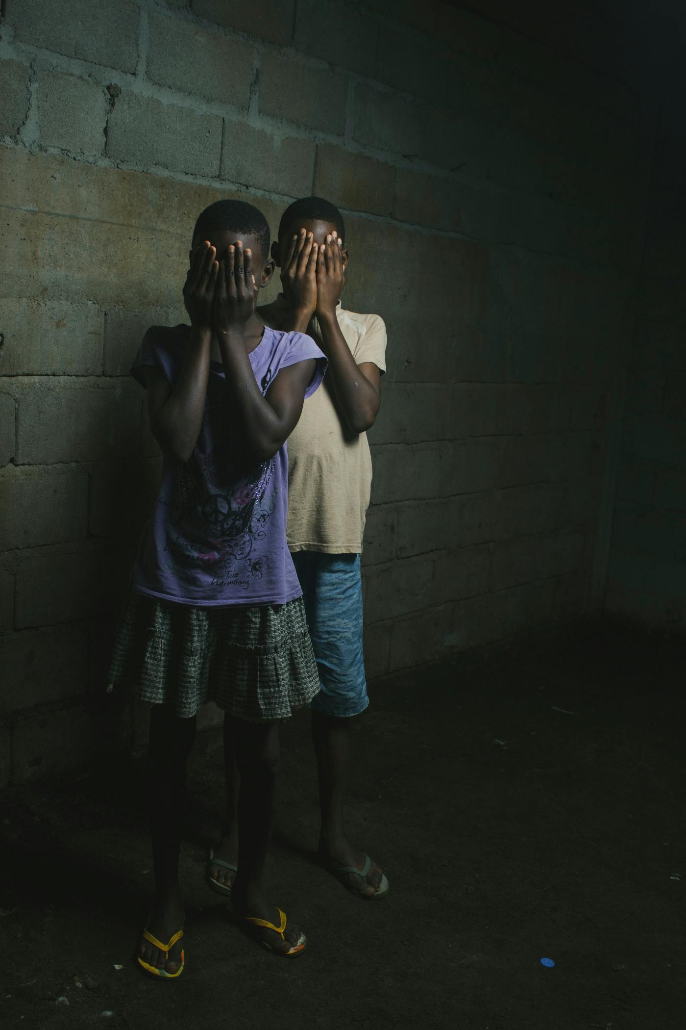 An African boy and girl covering their faces with their hands.