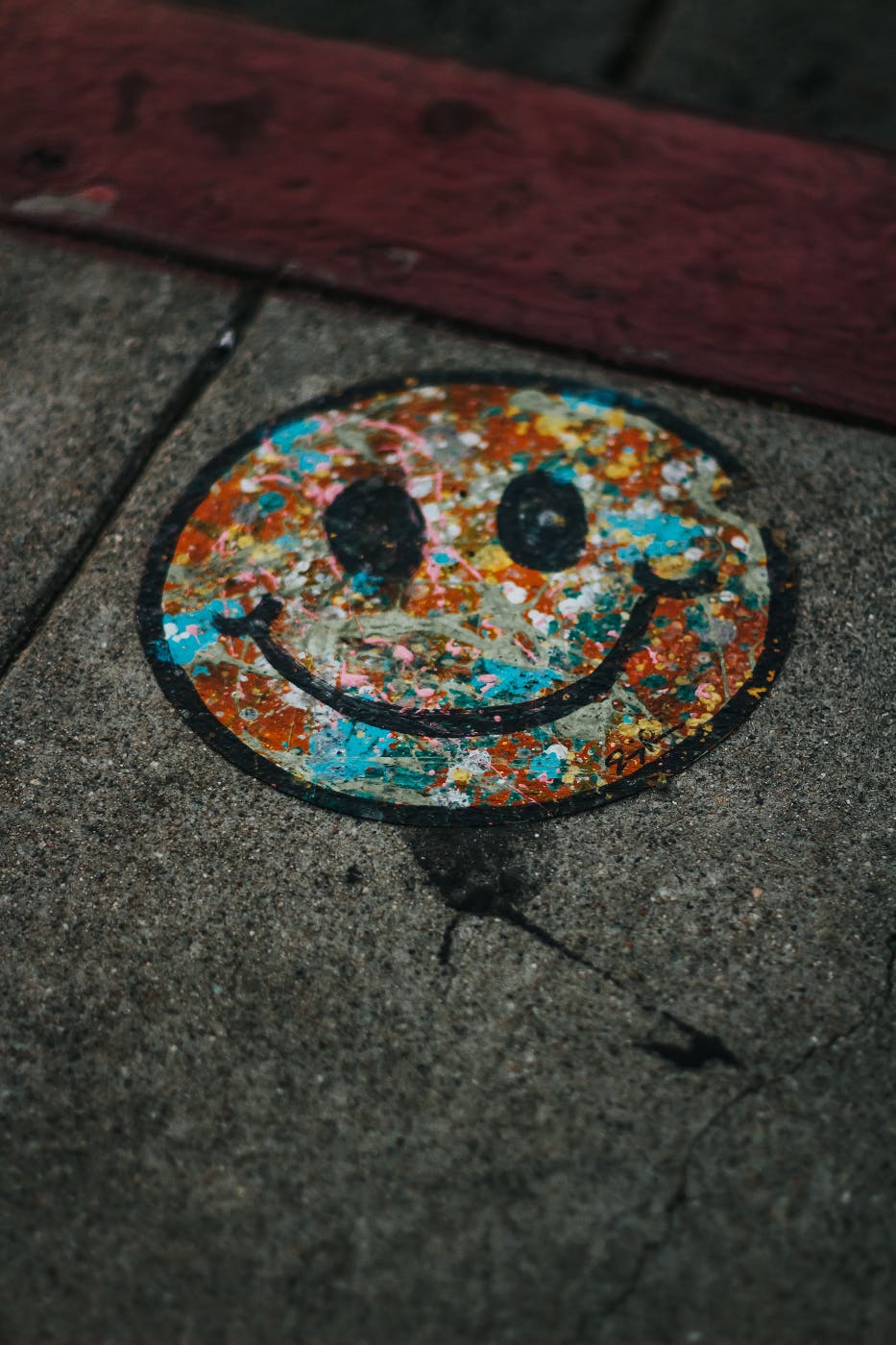 A multi-colored smiley face painted on a sidewalk