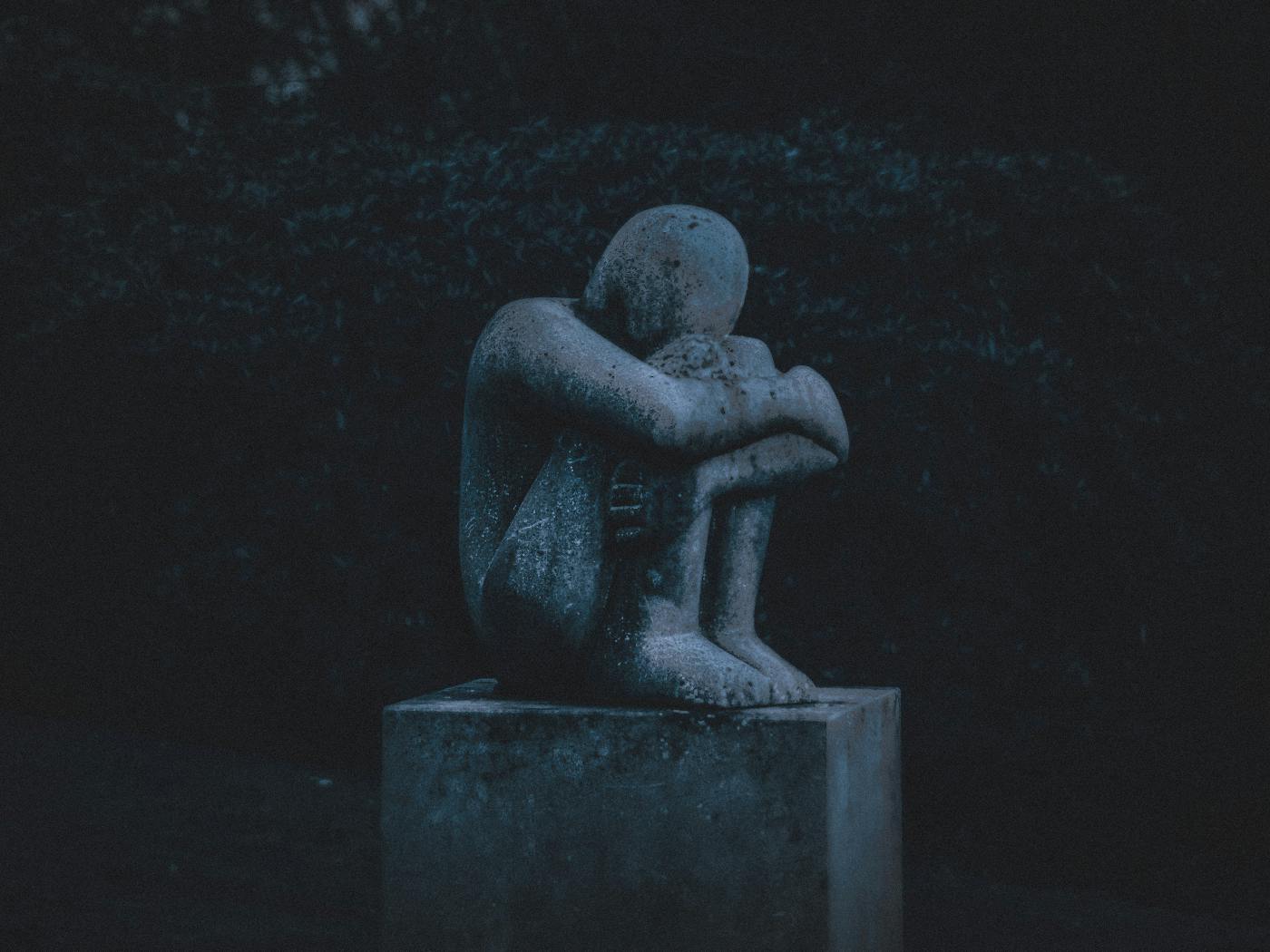 A statue of a person sitting, hugging their knees with their head down