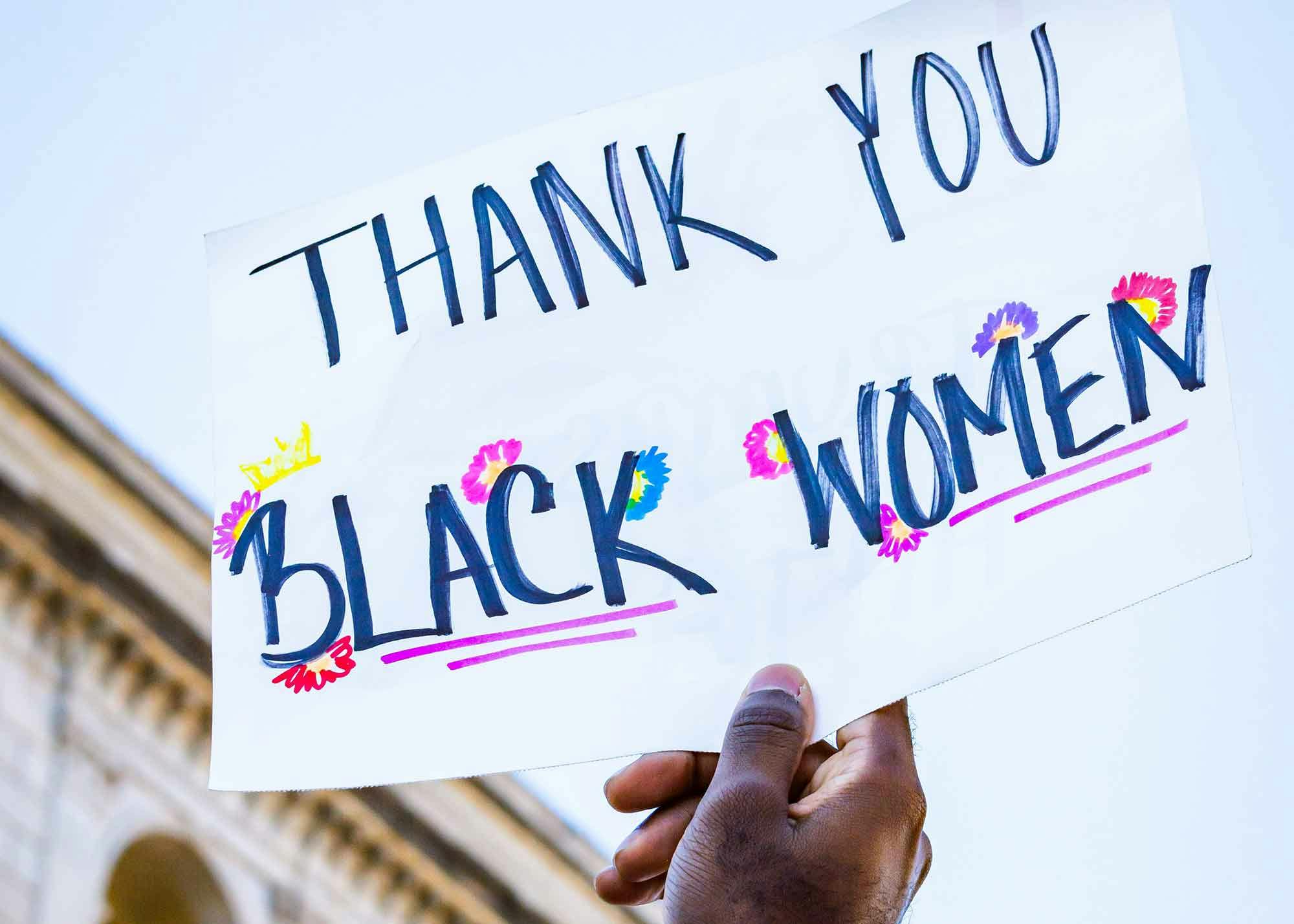 Woman holding a sign at a protest that reads "Thank you Black Women"