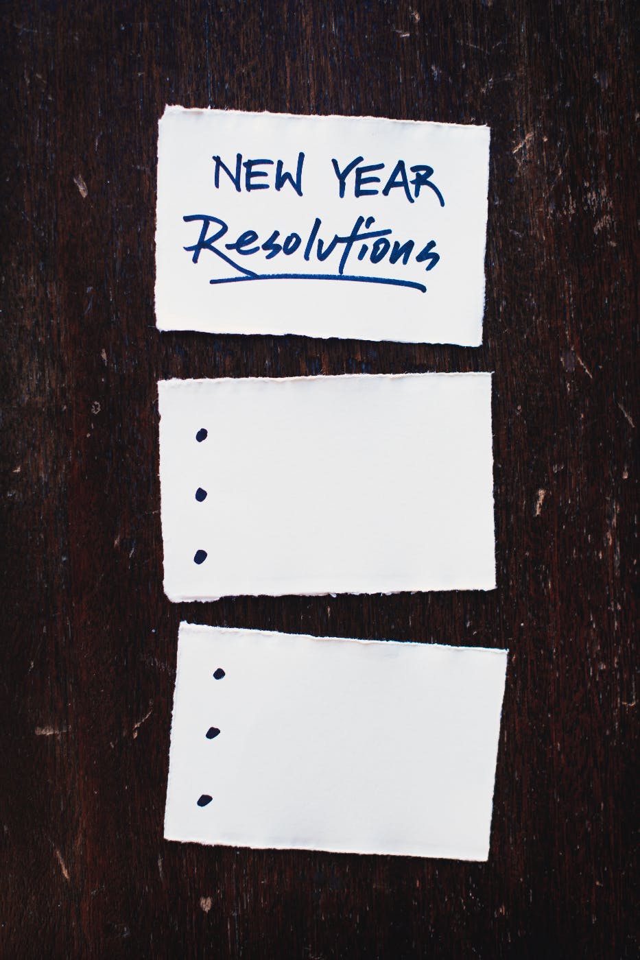 Three cards on a black table, top card reading: New Year Resolutions, the following two cards have three dots running down the left edge
