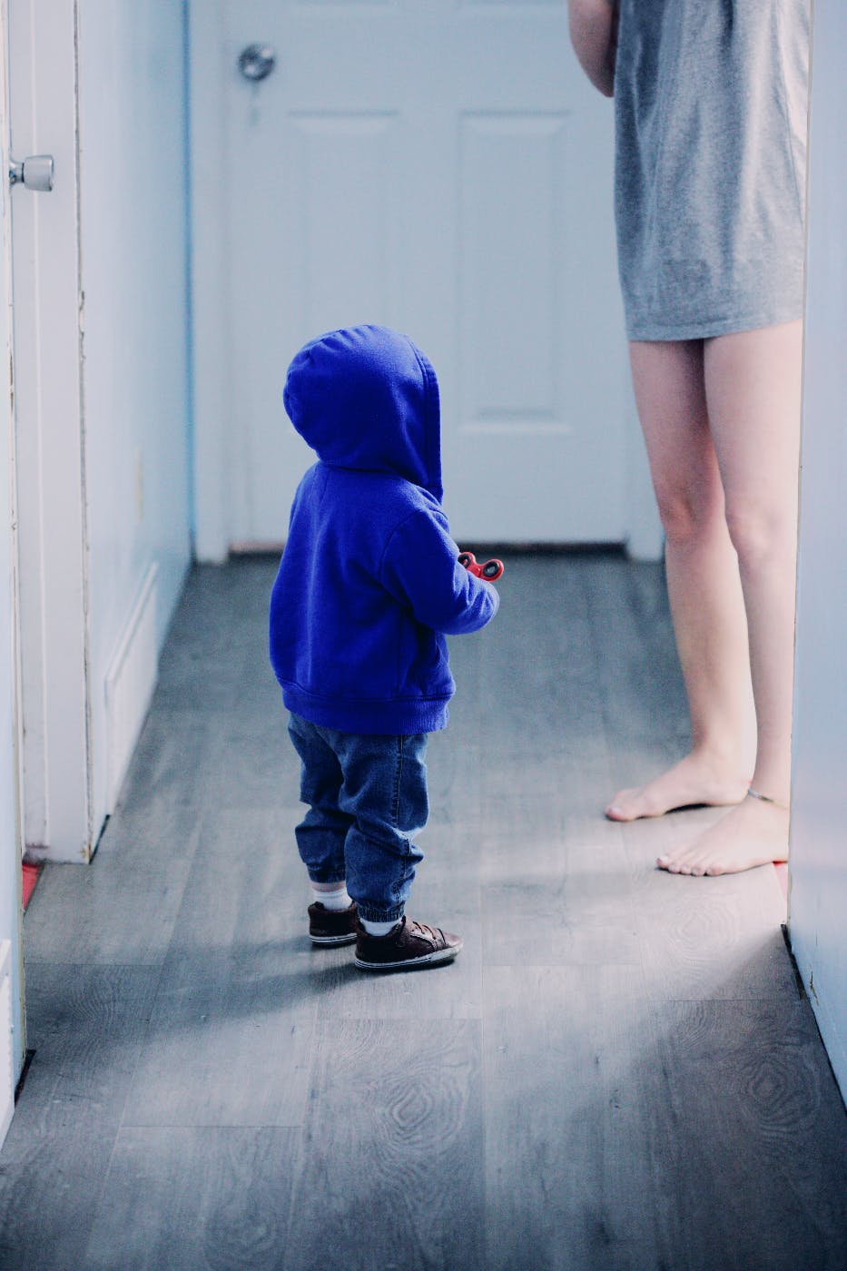 A toddler in a blue hoodie looking up at his mom