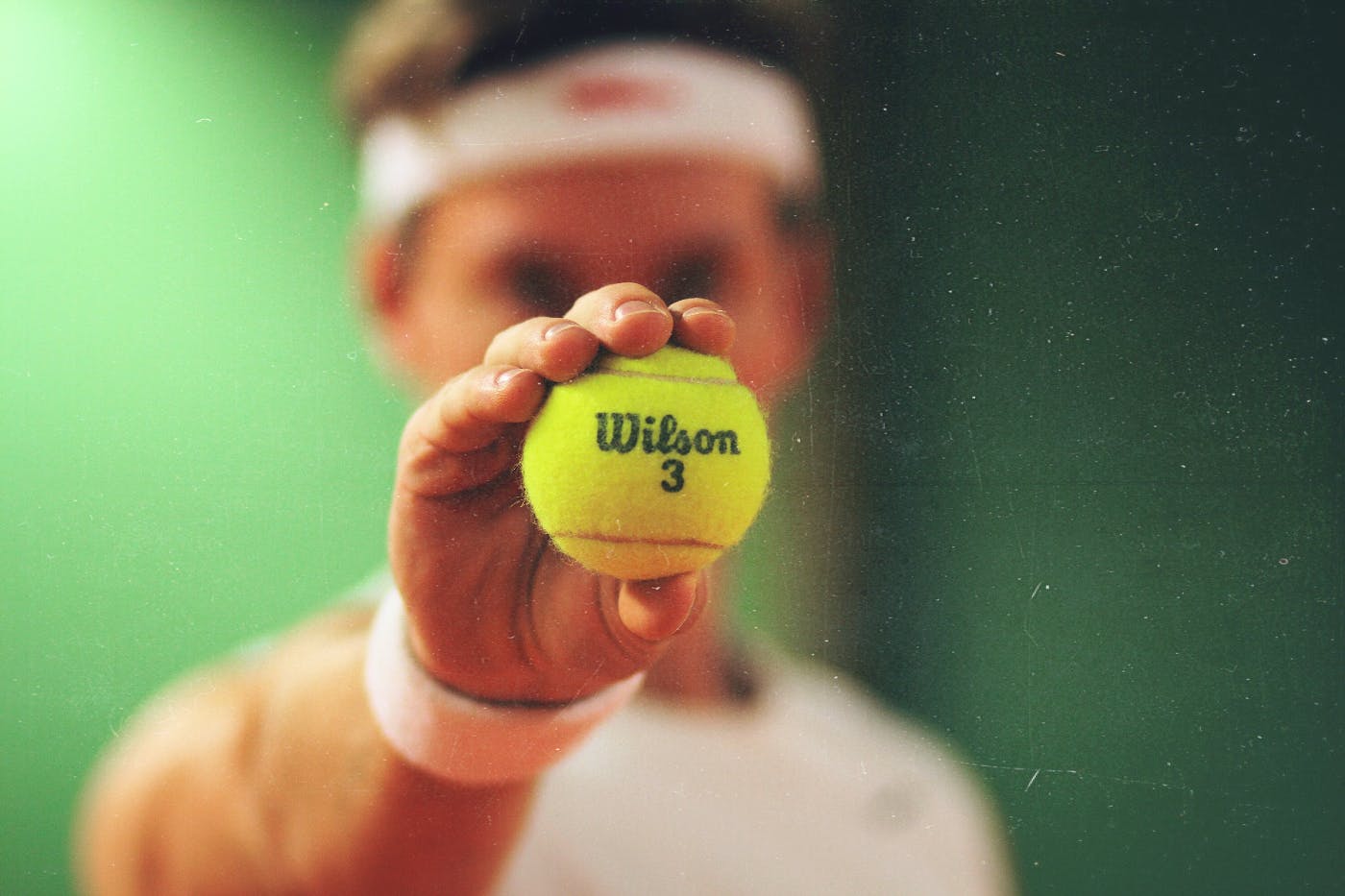 A tennis player holding a Wilson 3 ball toward the camera