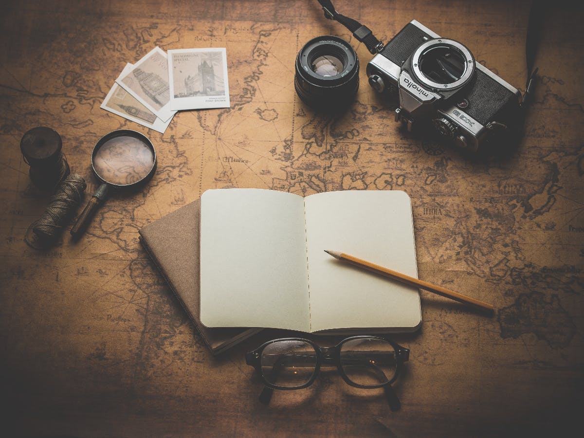 a desk with story telling items in it, a camera, a blaknk book, a pencil, eye glasses