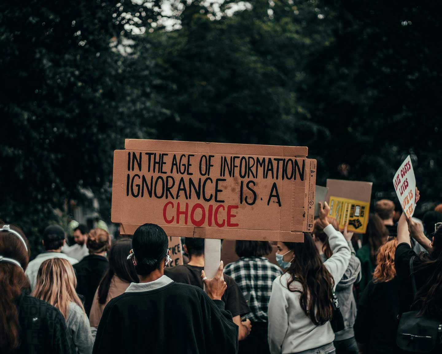Protester holding a sign that says "In the Age of Information, Ignorance is a Choice"