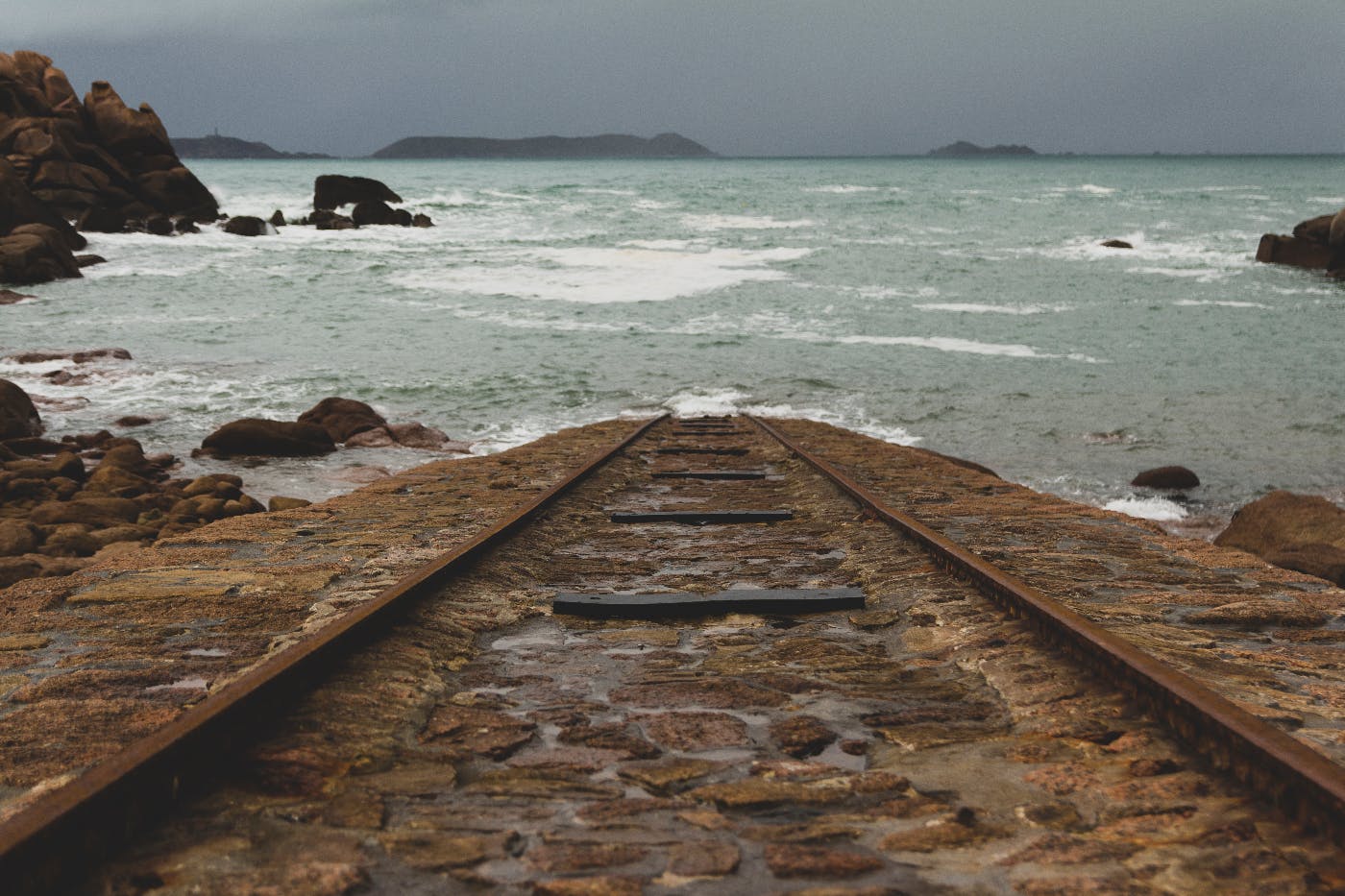 Rusted train tracks edning in the ocean.