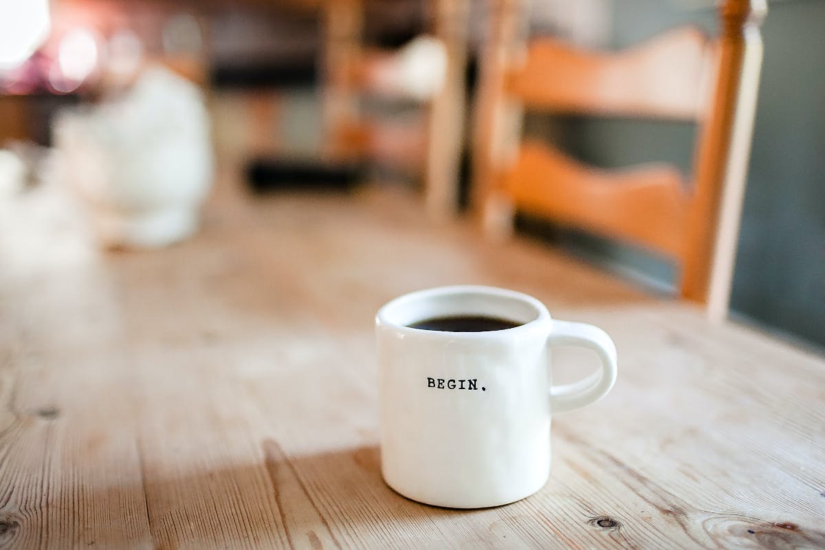 A coffee cup with thw word begin on it sitting on a wood kitchen table