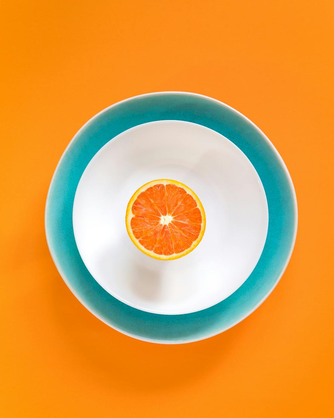 Half an orange sitting in a white bowl, on top of  a blue plate, on top of an orange background
