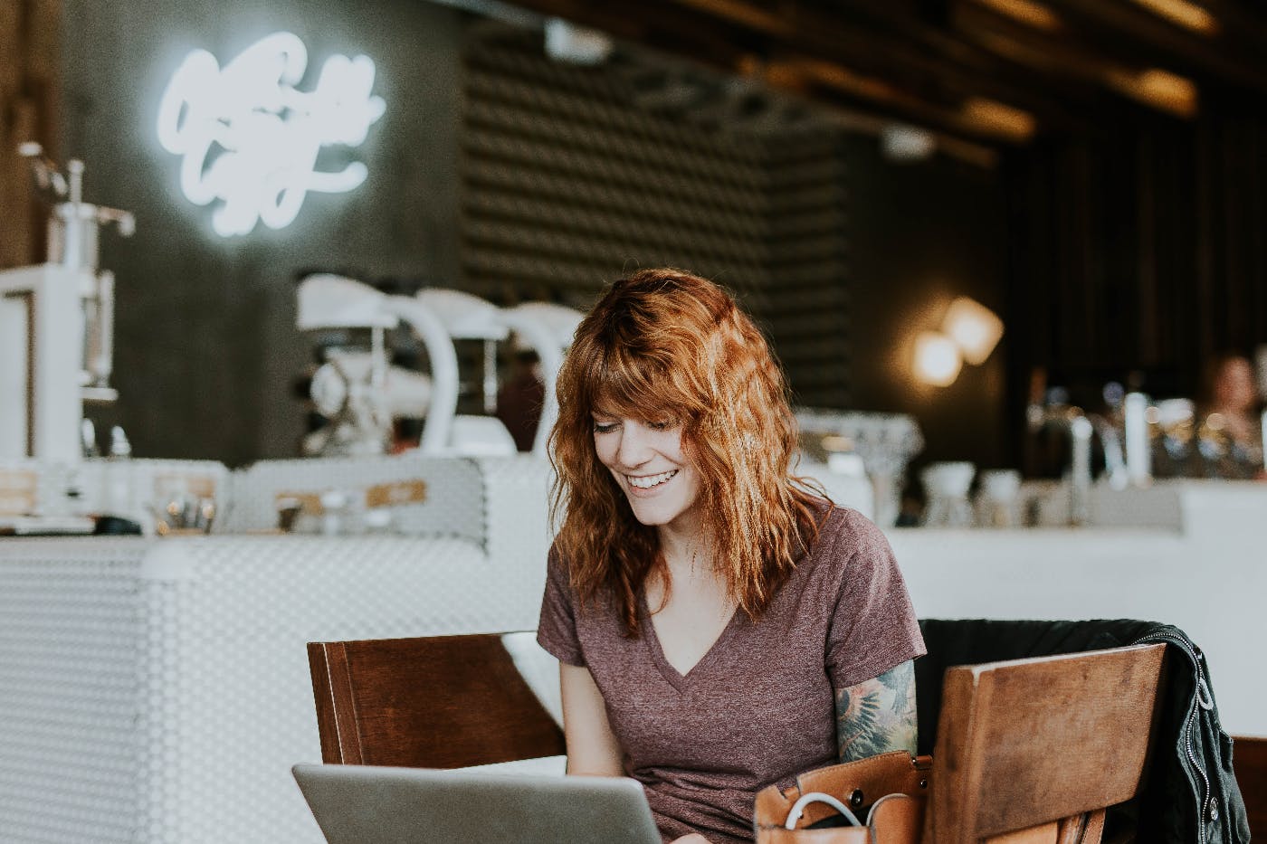 a woman with red hair in a coffee shop working on her laptop