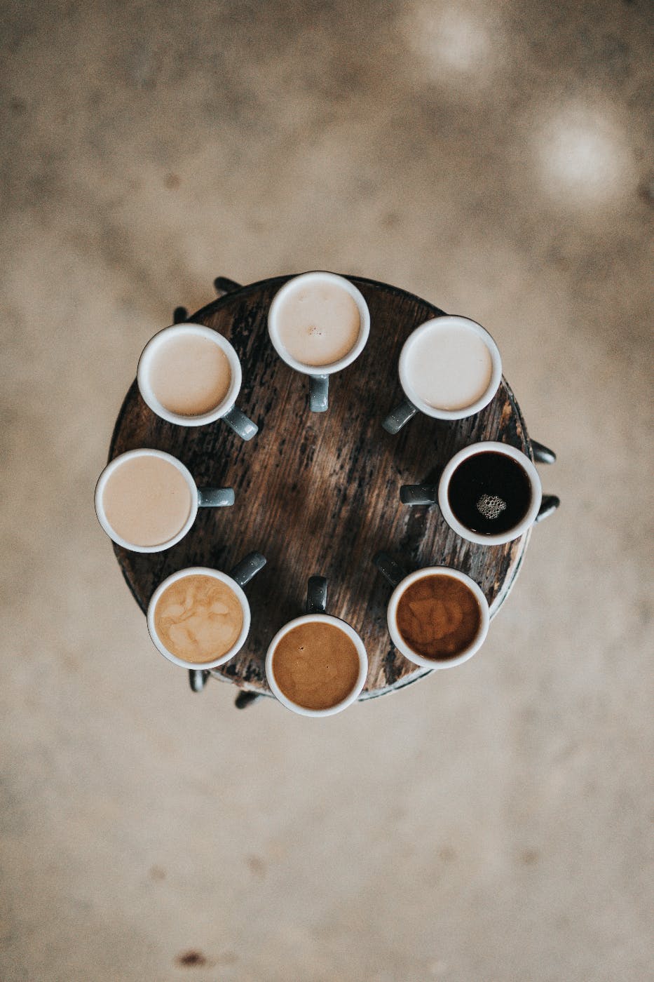  8 cups of coffee in varying colors in a circle on a round table