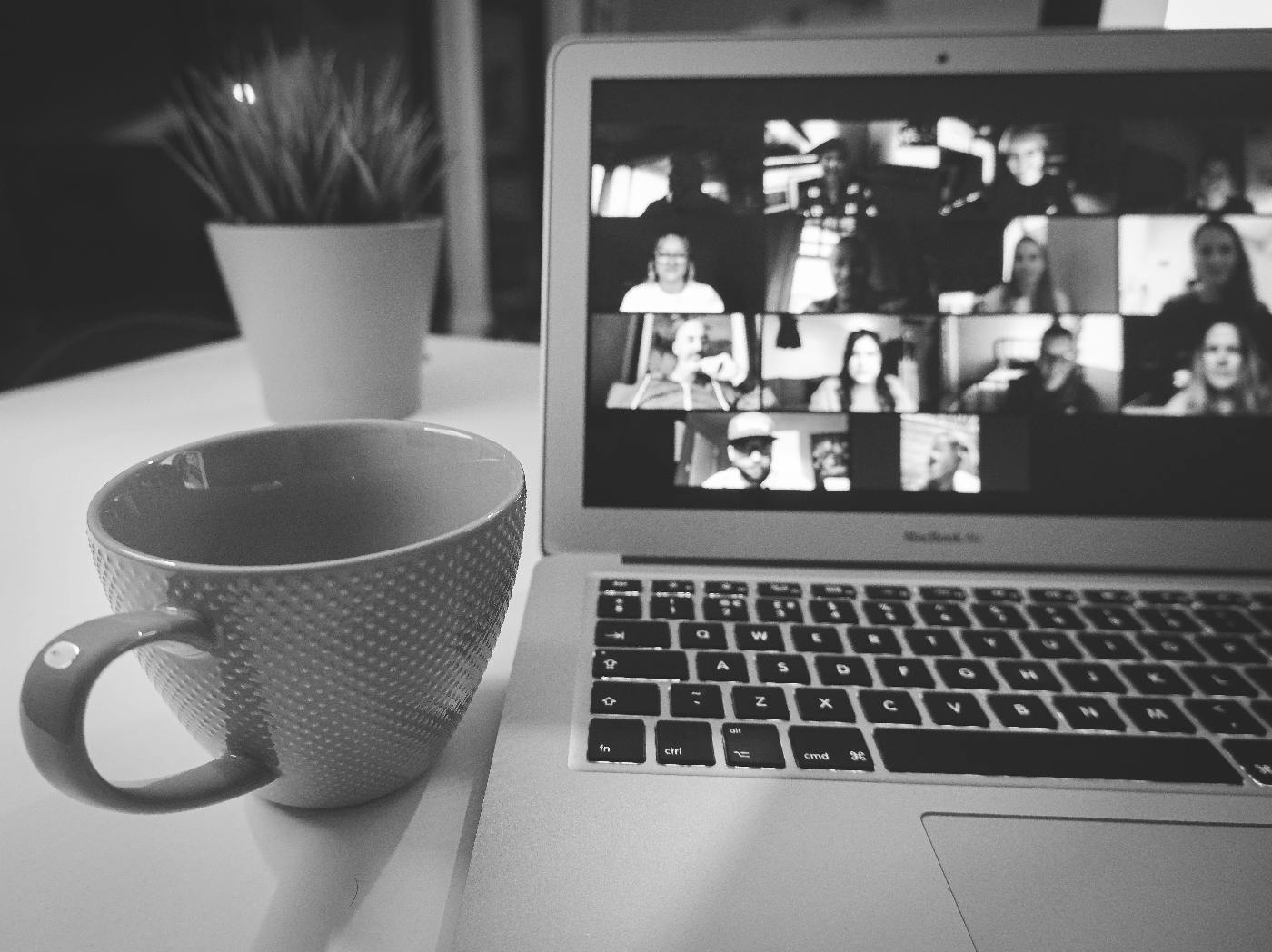 A coffee cup ona table beside a laptop with a zoom meeting on it