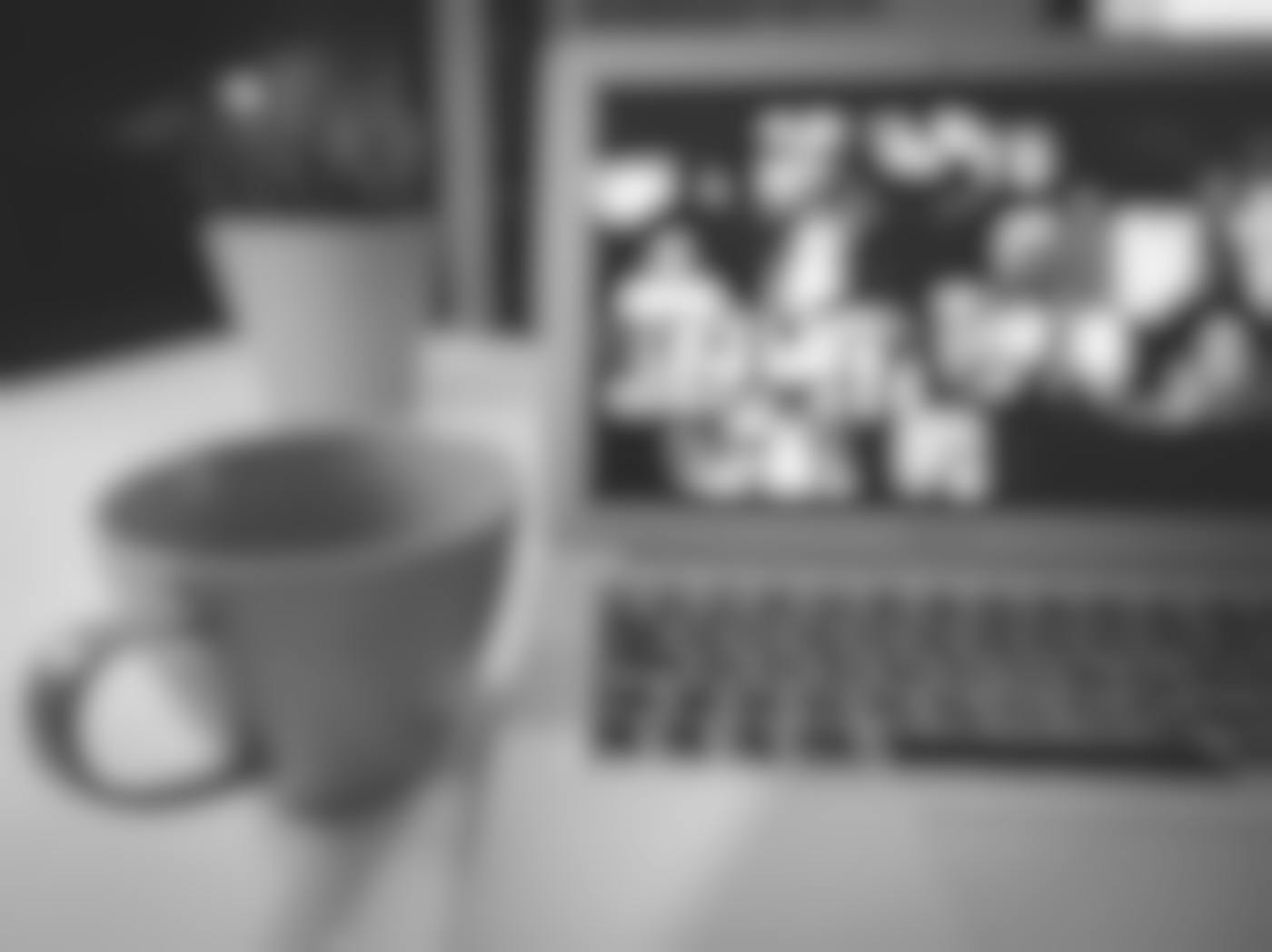 A coffee cup ona table beside a laptop with a zoom meeting on it