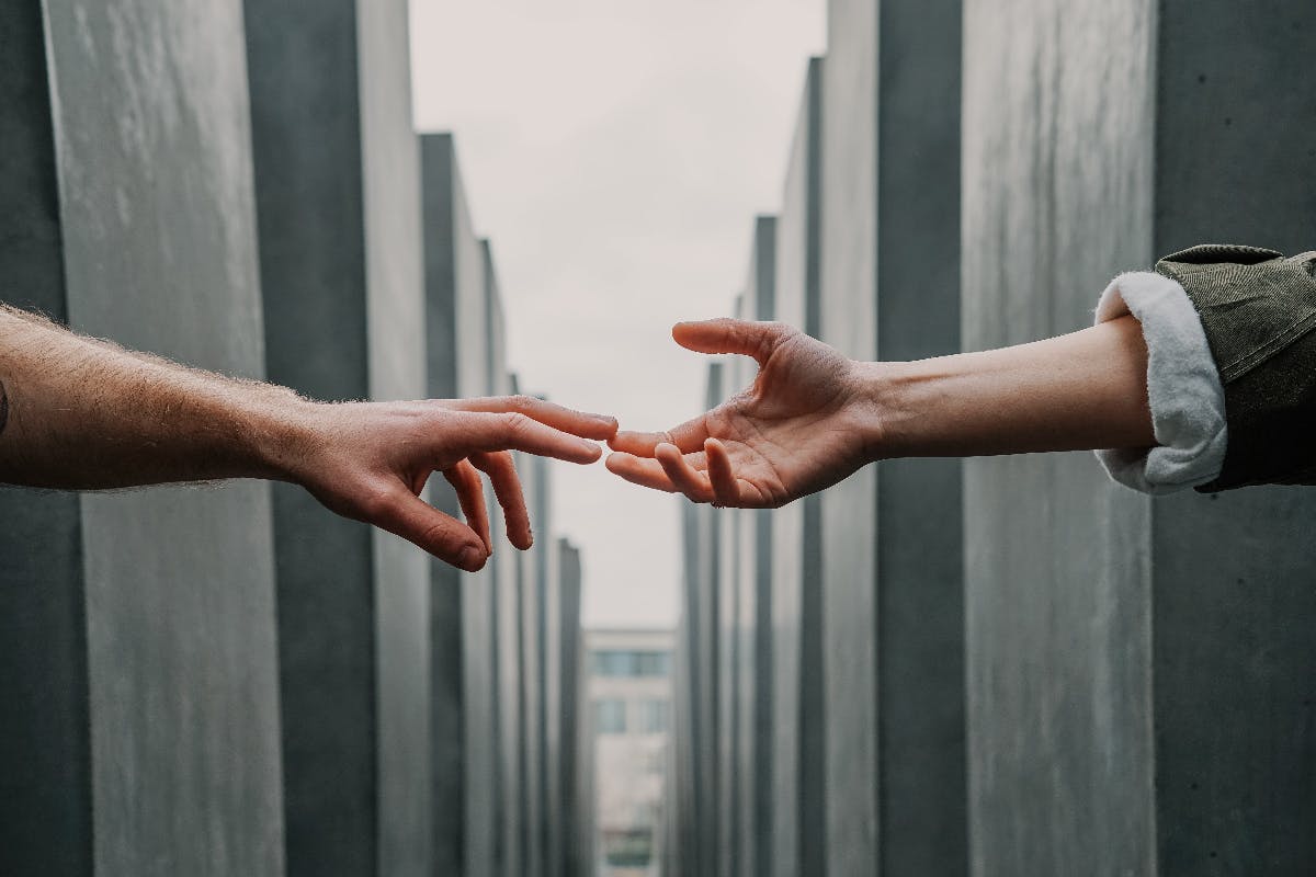 Two hands reaching out for each other among stone monolyths.